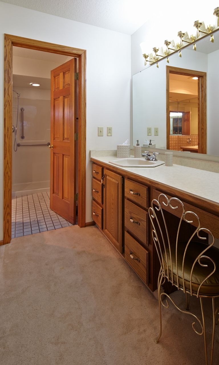 Un meuble-lavabo de maquillage désuet au fini chêne avec dessus de meuble-lavabo beige et lavabo.