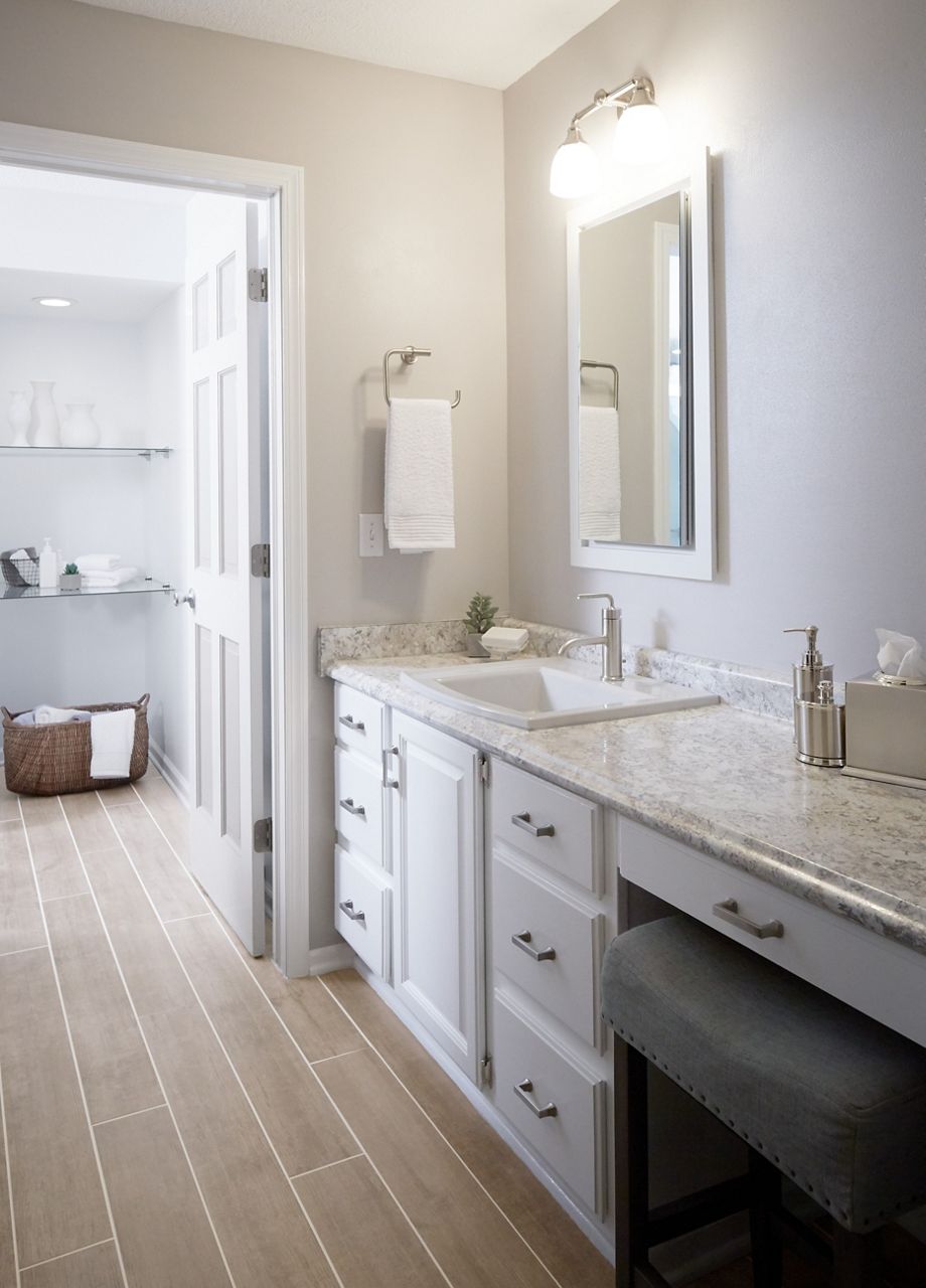 Le meuble-lavabo de maquillage refait en blanc, avec un dessus en granit, un lavabo Kohler blanc et un nouveau robinet élégant.