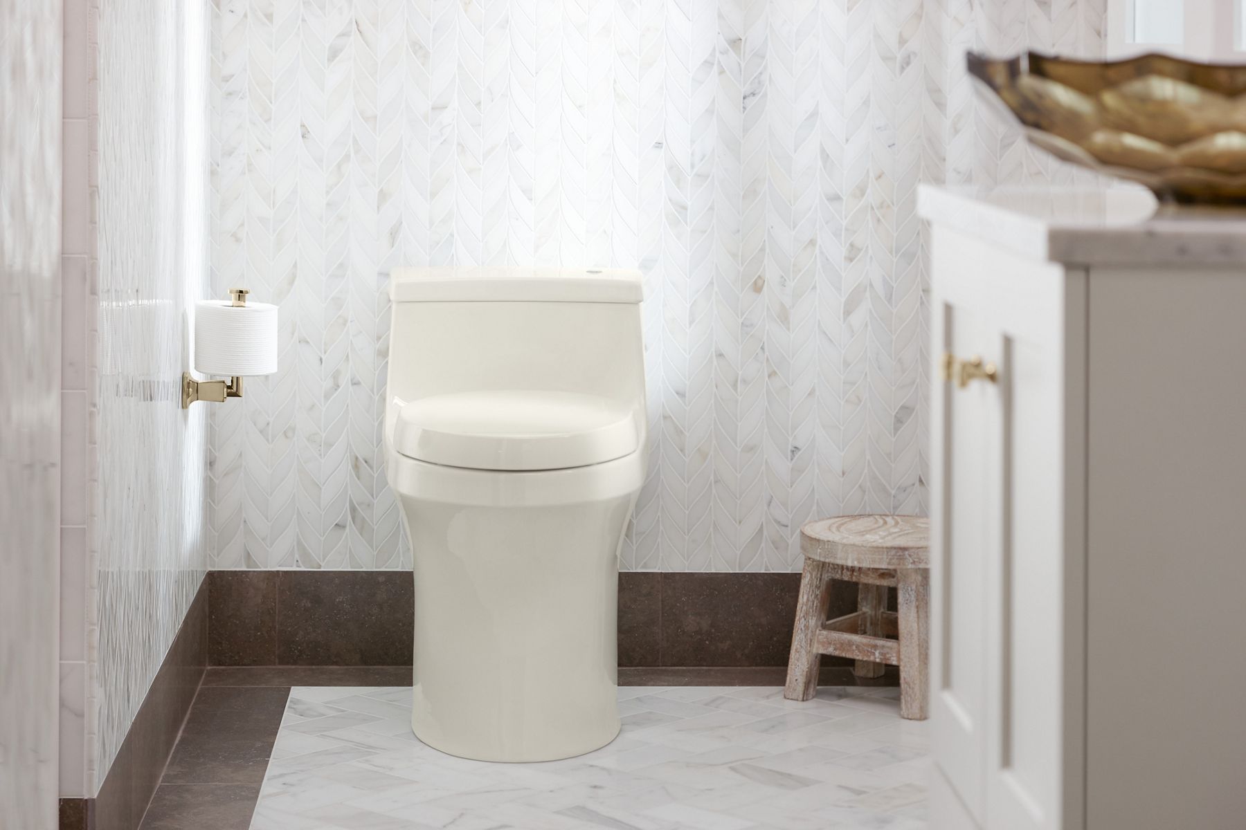 A biscuit colored toilet in a bathroom with light tiled walls with brown bases.