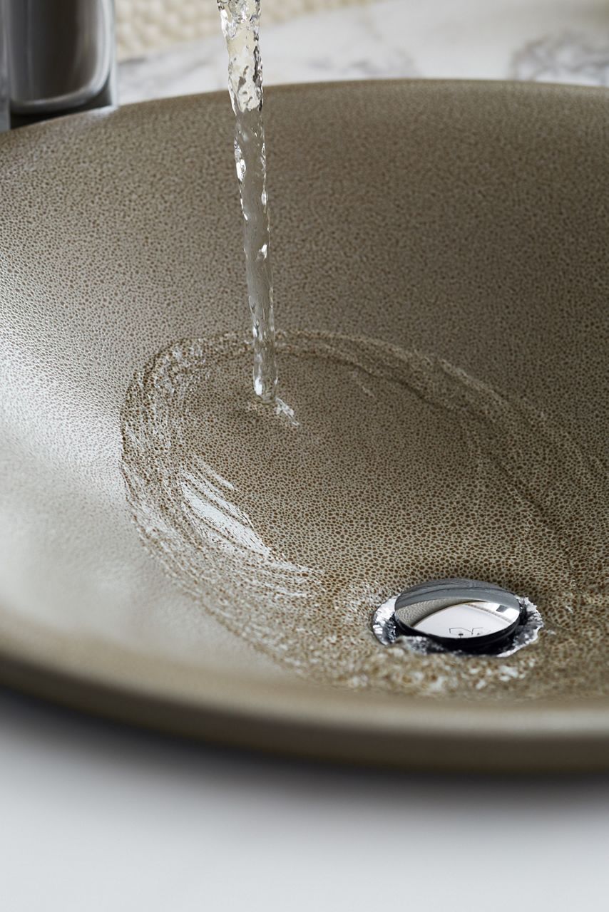 Close up detail of water pouring into a contemporary sink with a subtly textured surface.