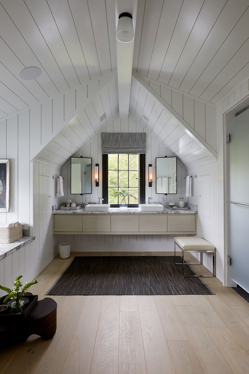 Une salle de bain nichée sous les avant-toits, avec des murs en tableau blanc, un meuble-lavabo mural, des lavabos en surface rectangulaires et des miroirs de chaque côté d’une fenêtre à cadre noir.