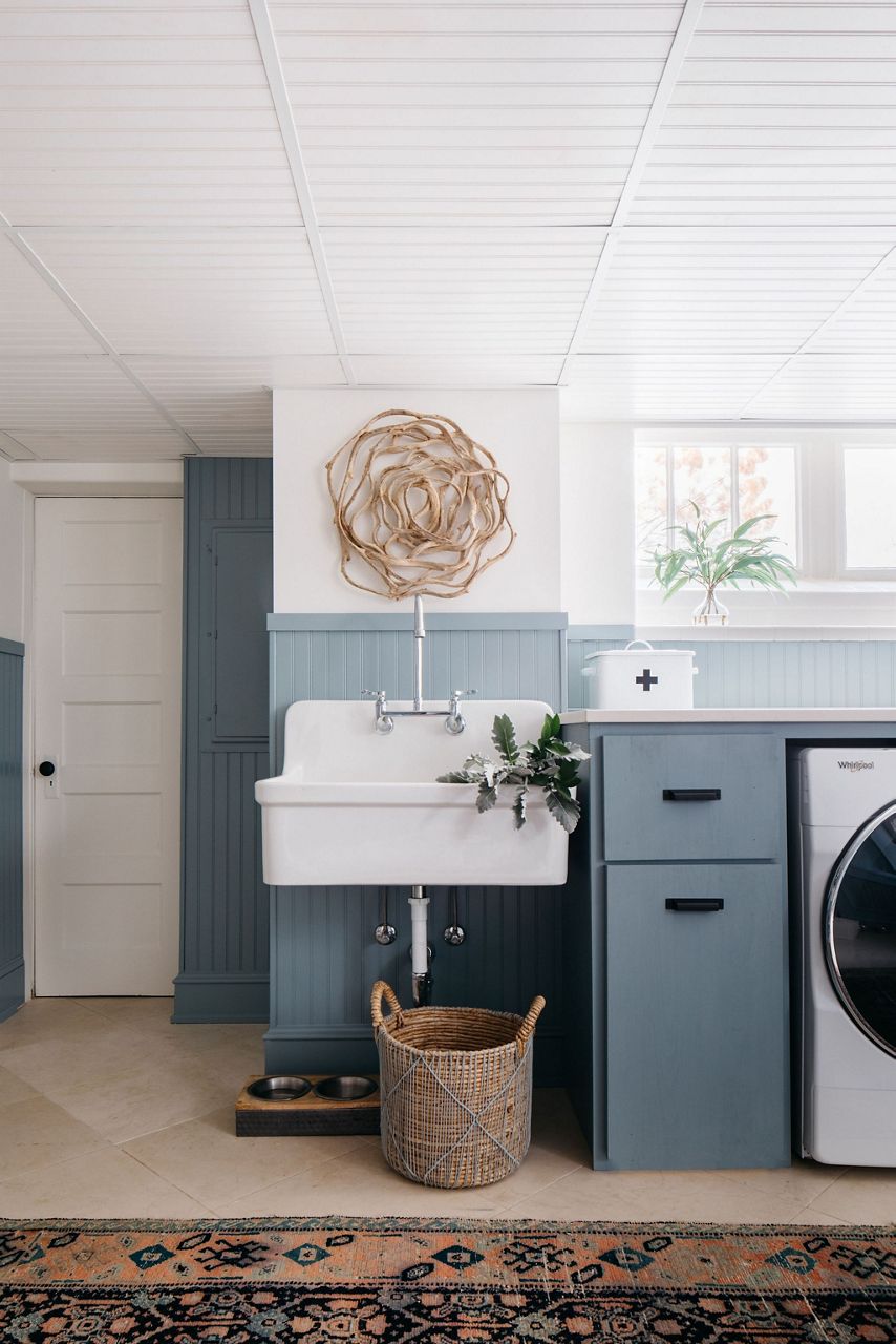 A laundry room with bluish gray cabinets and lower walls, white upper walls, and a basin sink. 