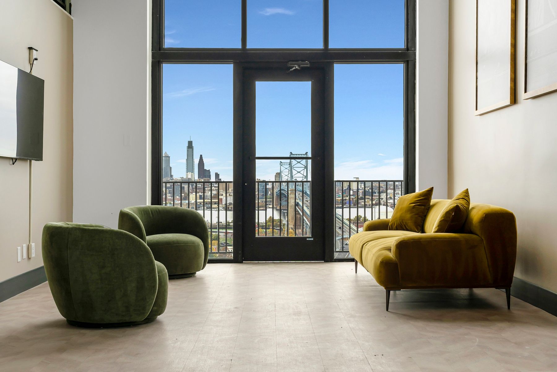 Floor to ceiling windows overlooking a city skyline in a room with plush chairs and sofa.
