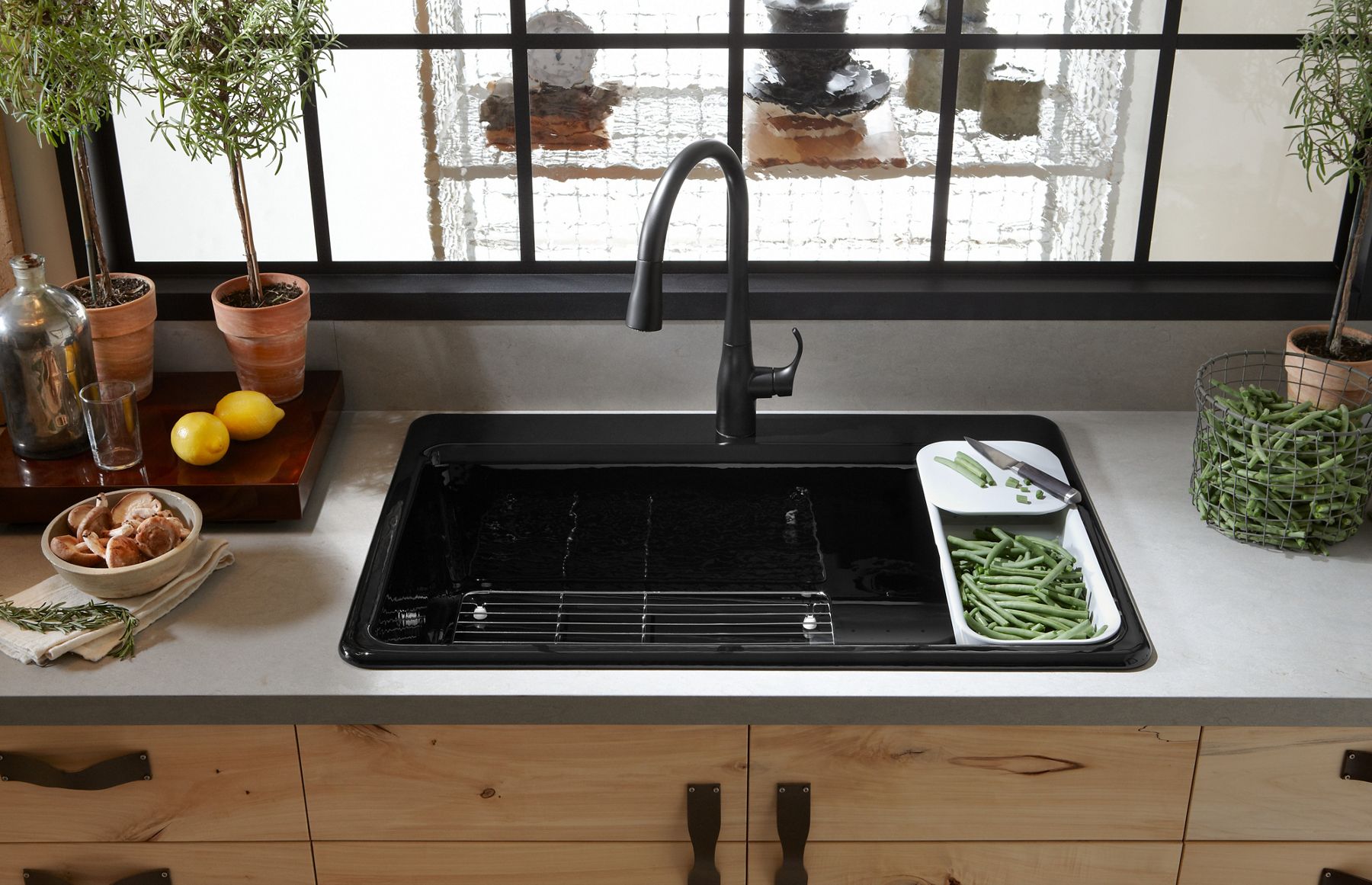 Fruits and vegetables sit on a white counter, next to a black KOHLER single bowl sink with built in strainer.