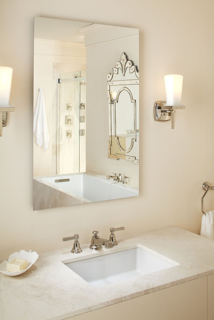 A large frameless KOHLER bathroom mirror is mounted above a white vanity with an undermount sink.
