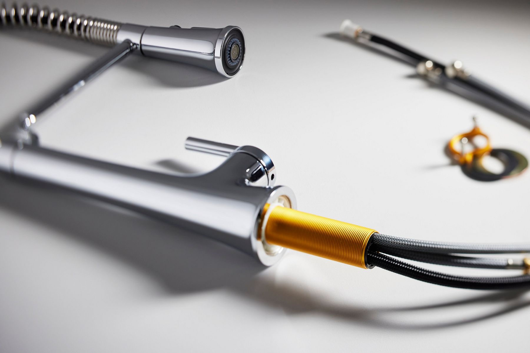 A kitchen faucet laying on a white table showing the water hoses and other installation components.