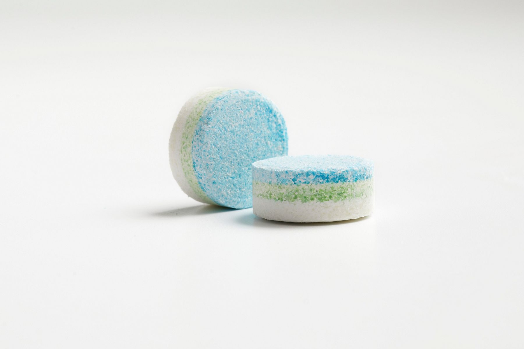 A close-up of two toilet cleaning tablets with blue, green, and white layers