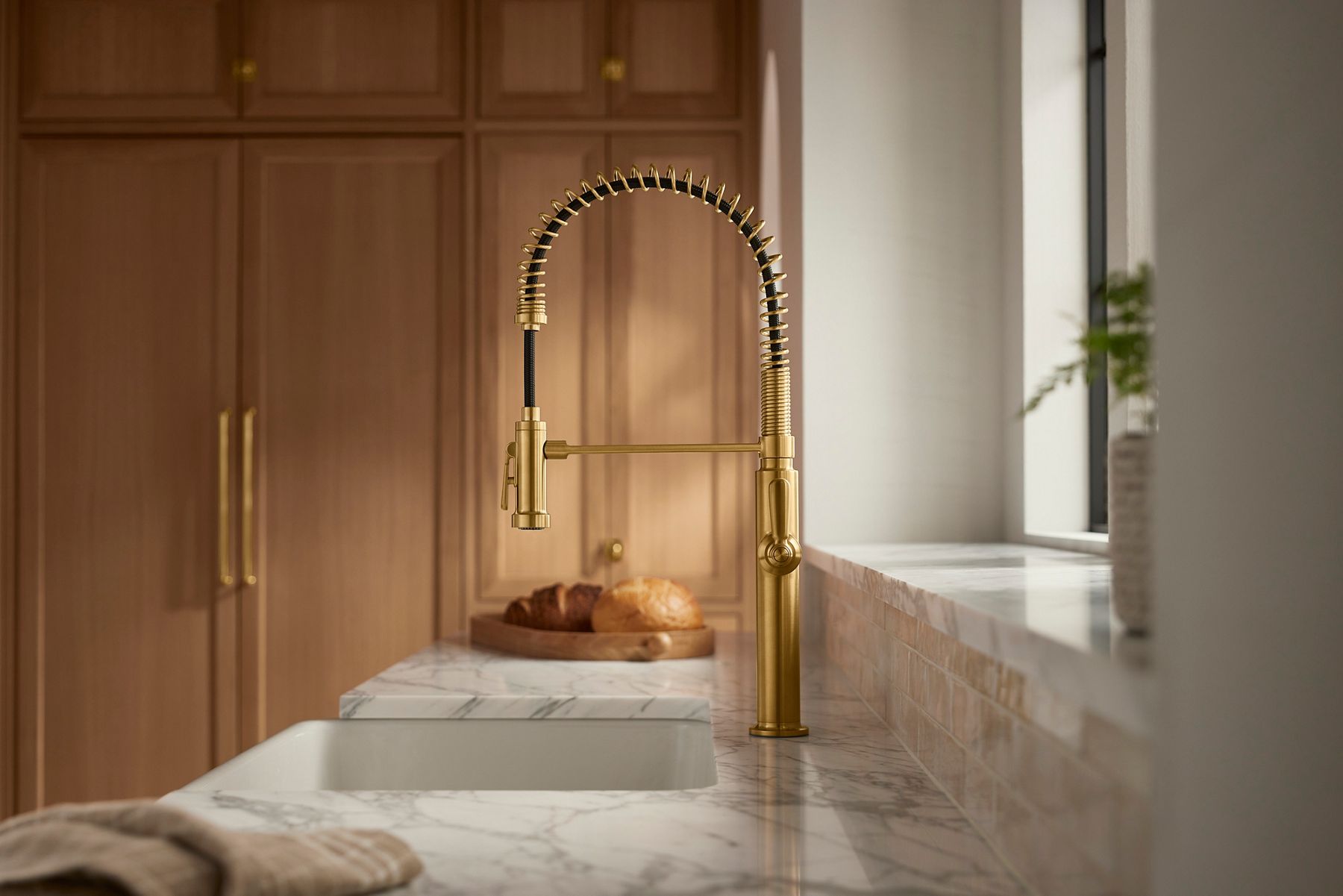 A close-up of a wall-mounted brass bathroom faucet with cross handles and curved spout installed above a veined marble back-splash and integrated sink