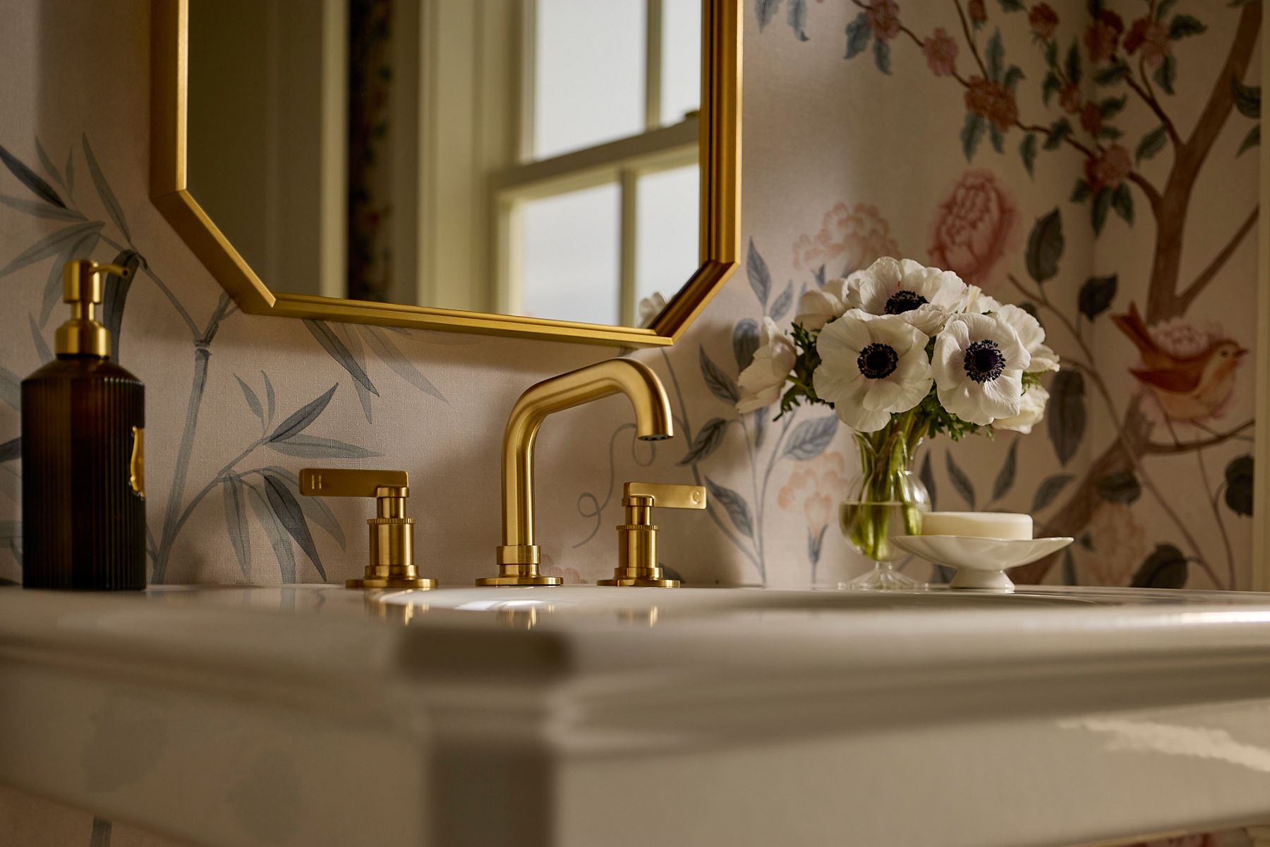 A gold-toned faucet in a bright white kitchen next to a matching mirror.