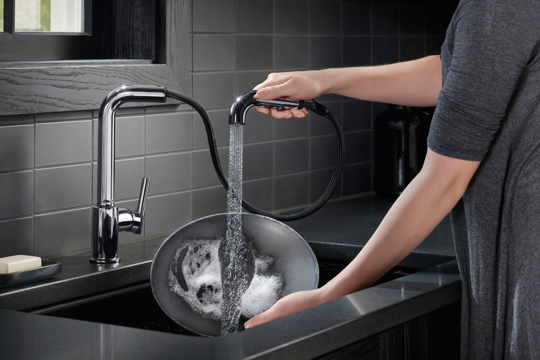A person rinsing out a dish in a sink while holding a faucet with its spout pulled out from the base to provide better reach.