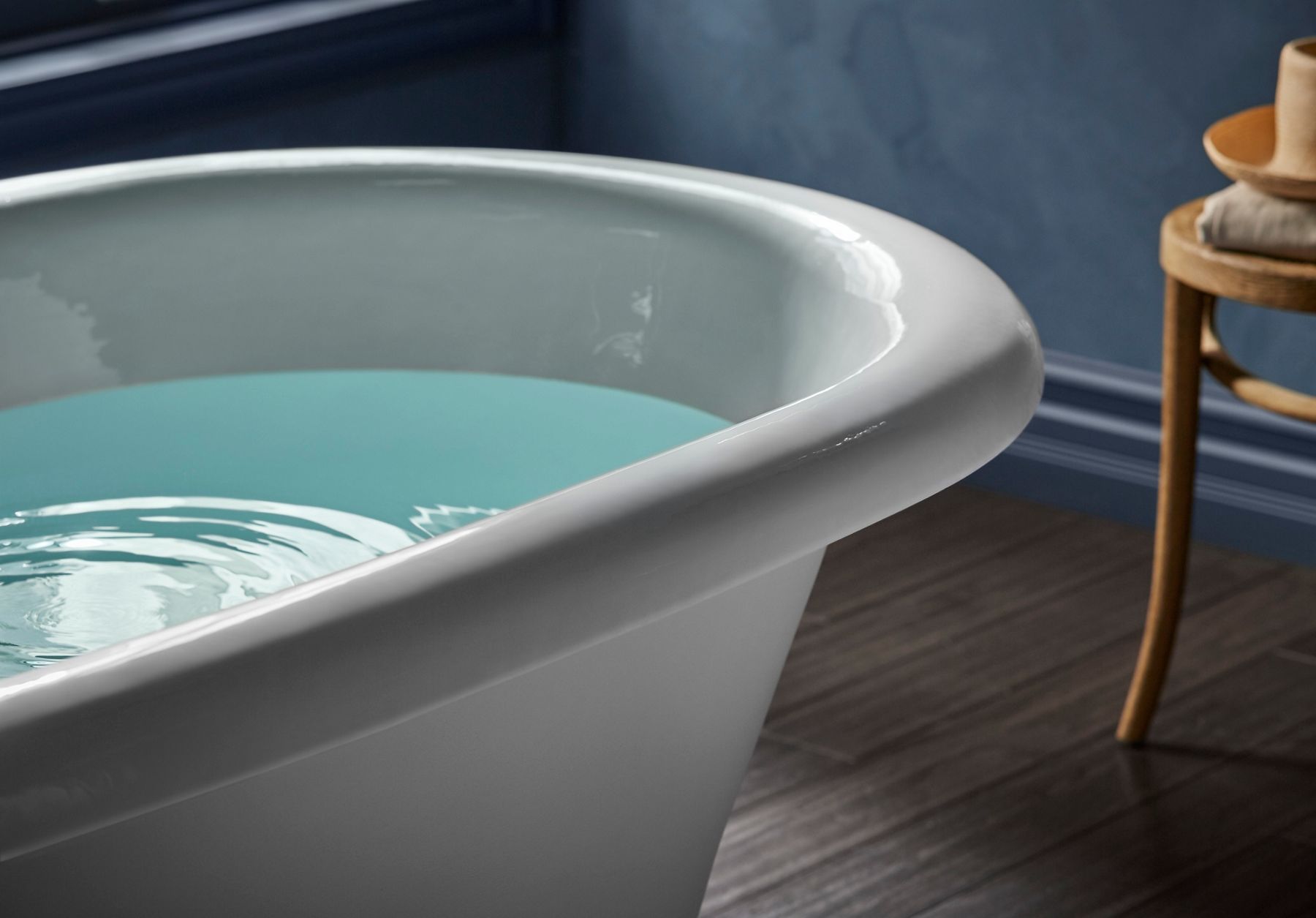 A close-up of a white, enameled cast iron bathtub filled with water on a wood floor