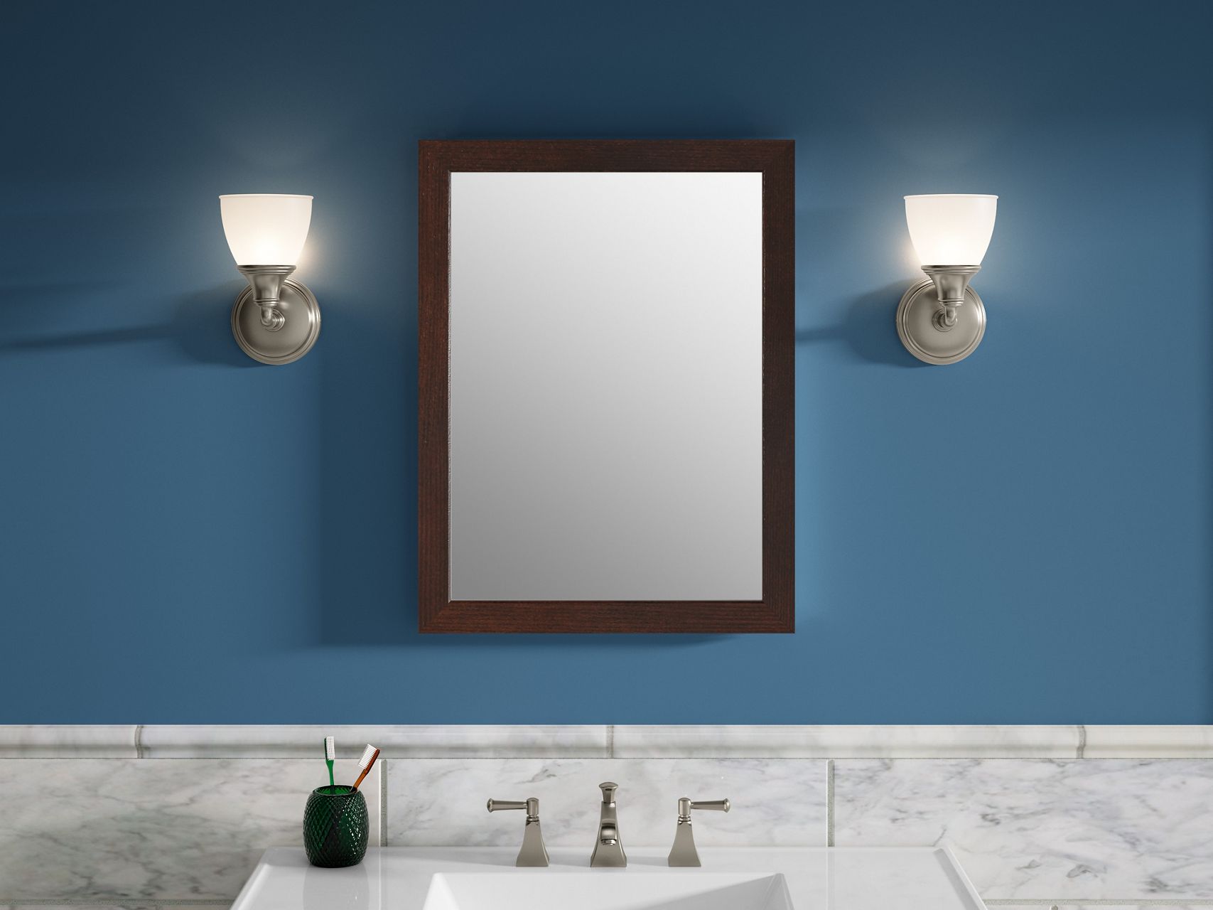 A KOHLER Tresham framed mirror in Woodland hangs between two sconces against a blue bathroom wall, above a white vanity and sink.