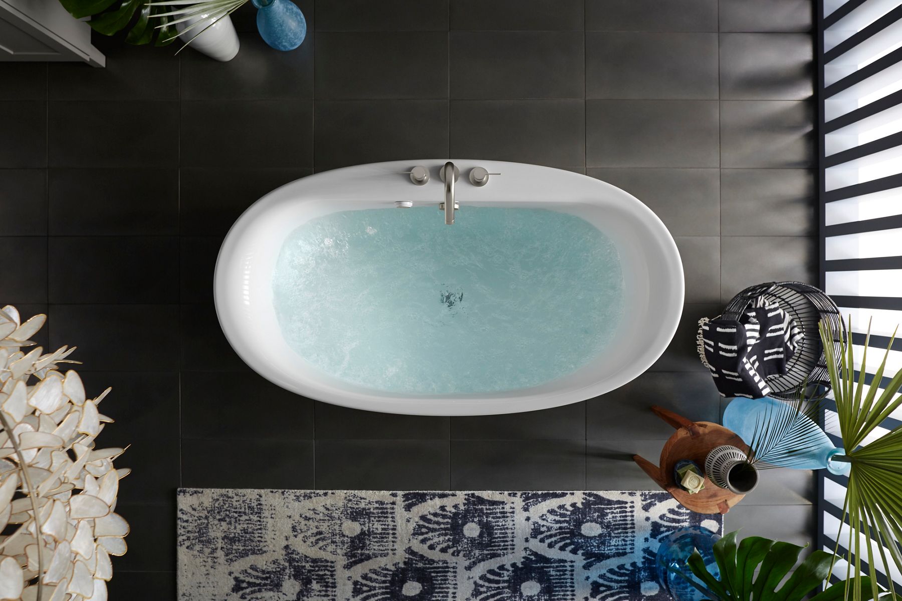 An overhead view of a  white, lithocast and acrylic bathtub with chrome faucet and filled with water
