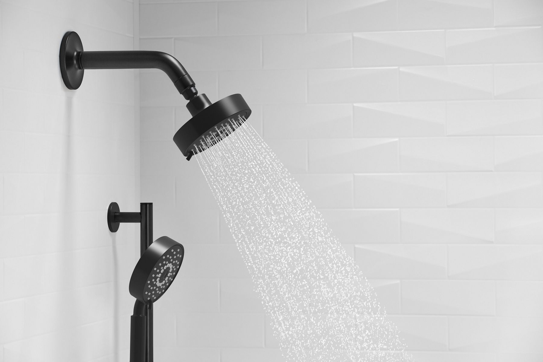 A close-up of black showerhead with water and black handshower, backed by white tile