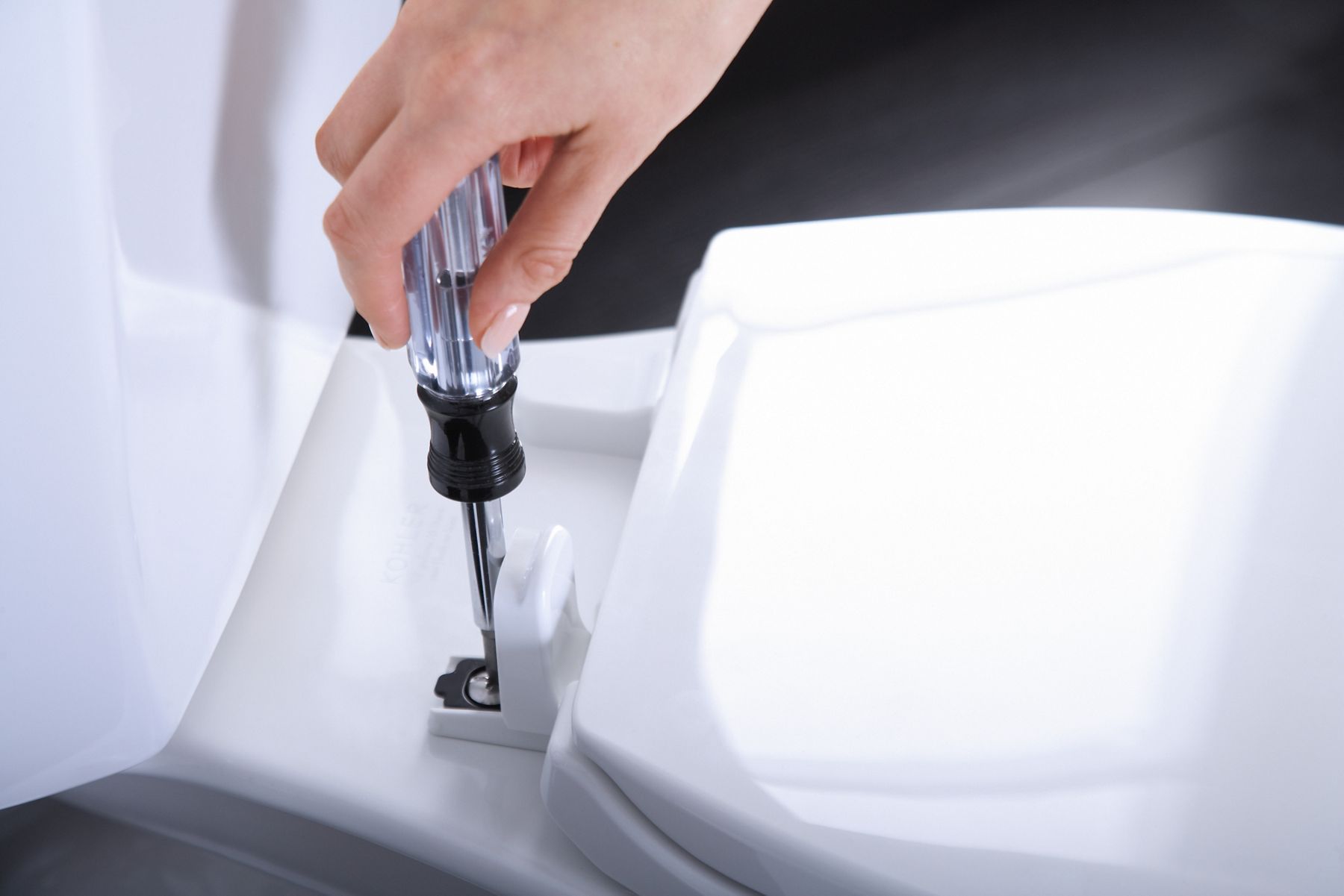 A person uses a screwdriver to install a KOHLER Brevia toilet seat.