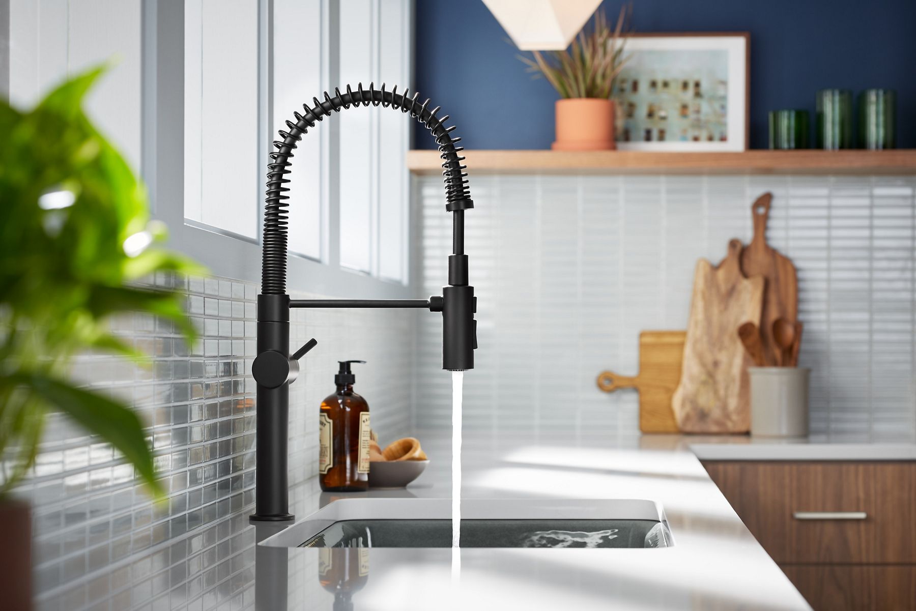 A KOHLER Crue pull-down faucet over a white farmhouse sink installed in an island with dark cabinets.