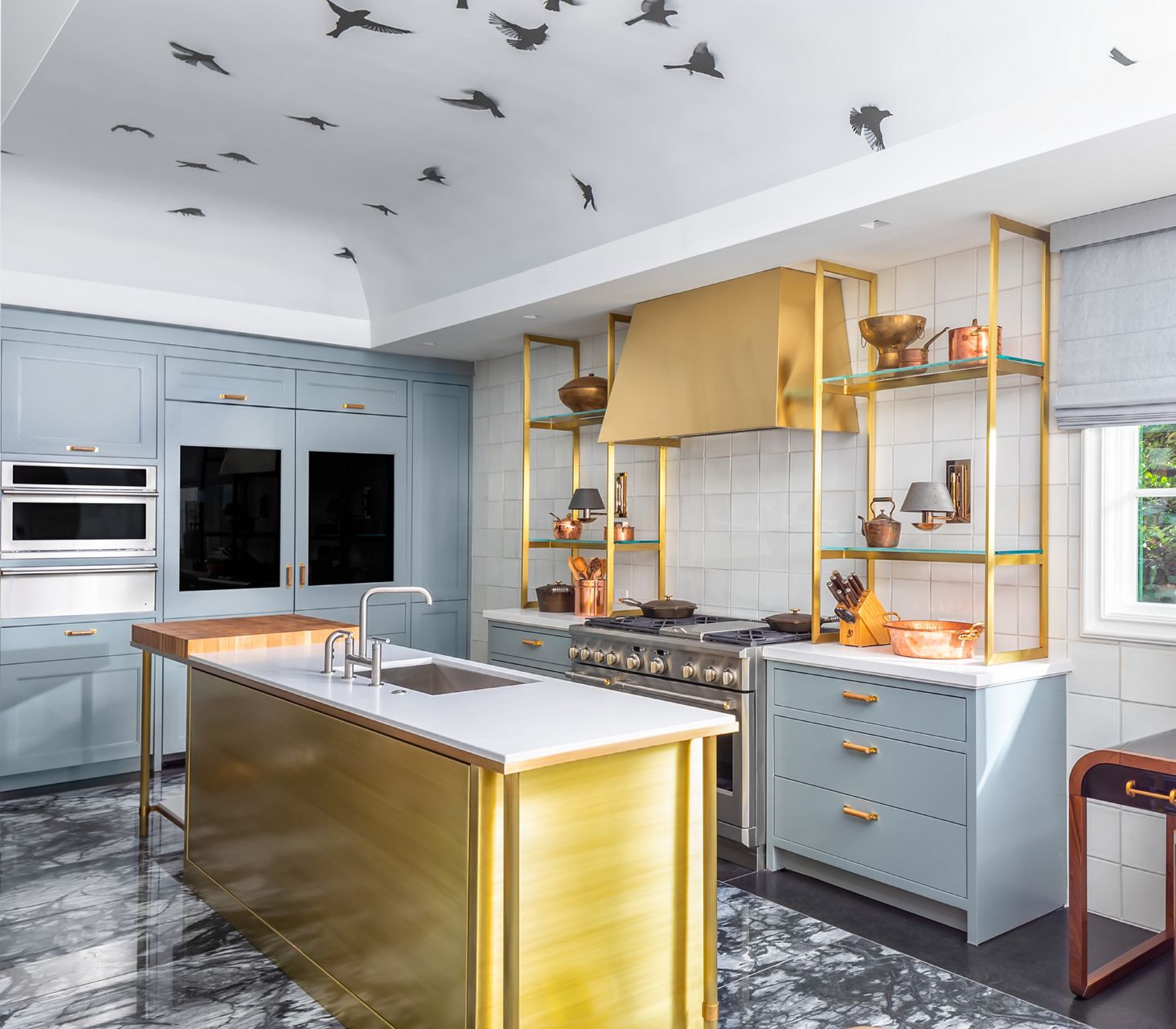 A kitchen in tones of baby blue and golden yellow with an island and stick-on birds on the ceiling.