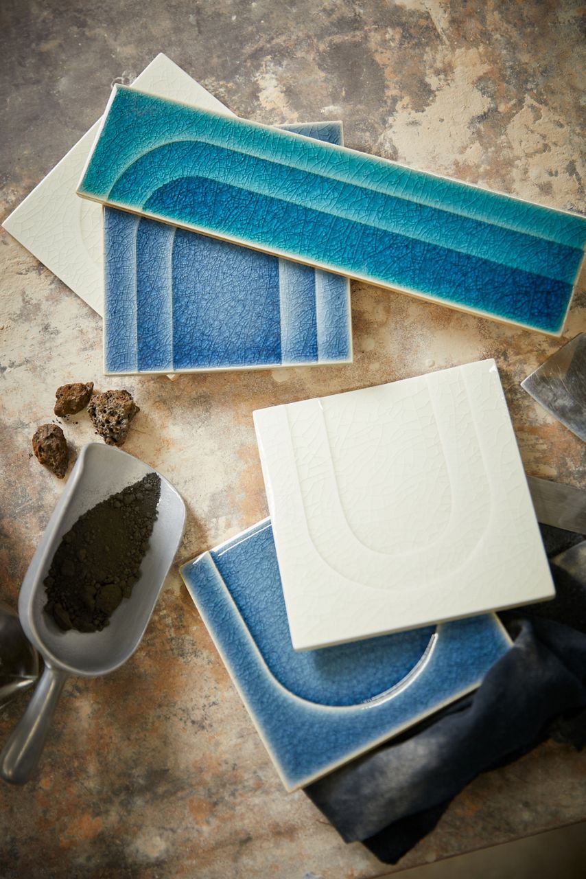 Tiles laying on a table in varying shades of blue and one tile in bone finish.