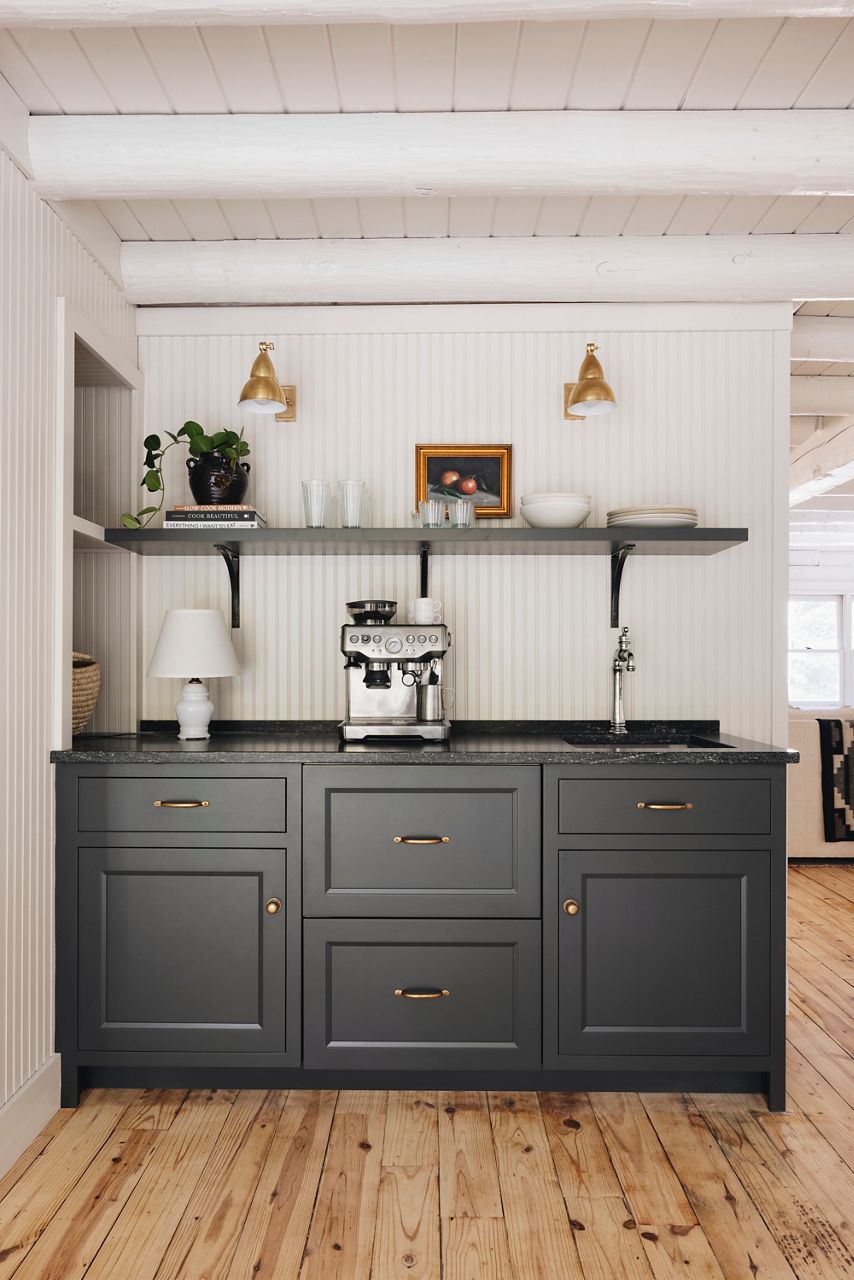 Centered in the image is the coffee bar space which features a dark-blue cabinet base and matching wall shelf on the white beadboard wall. There is a chrome coffee maker in the center of the counter top next to the undermounted bar sink and single handle beverage faucet.