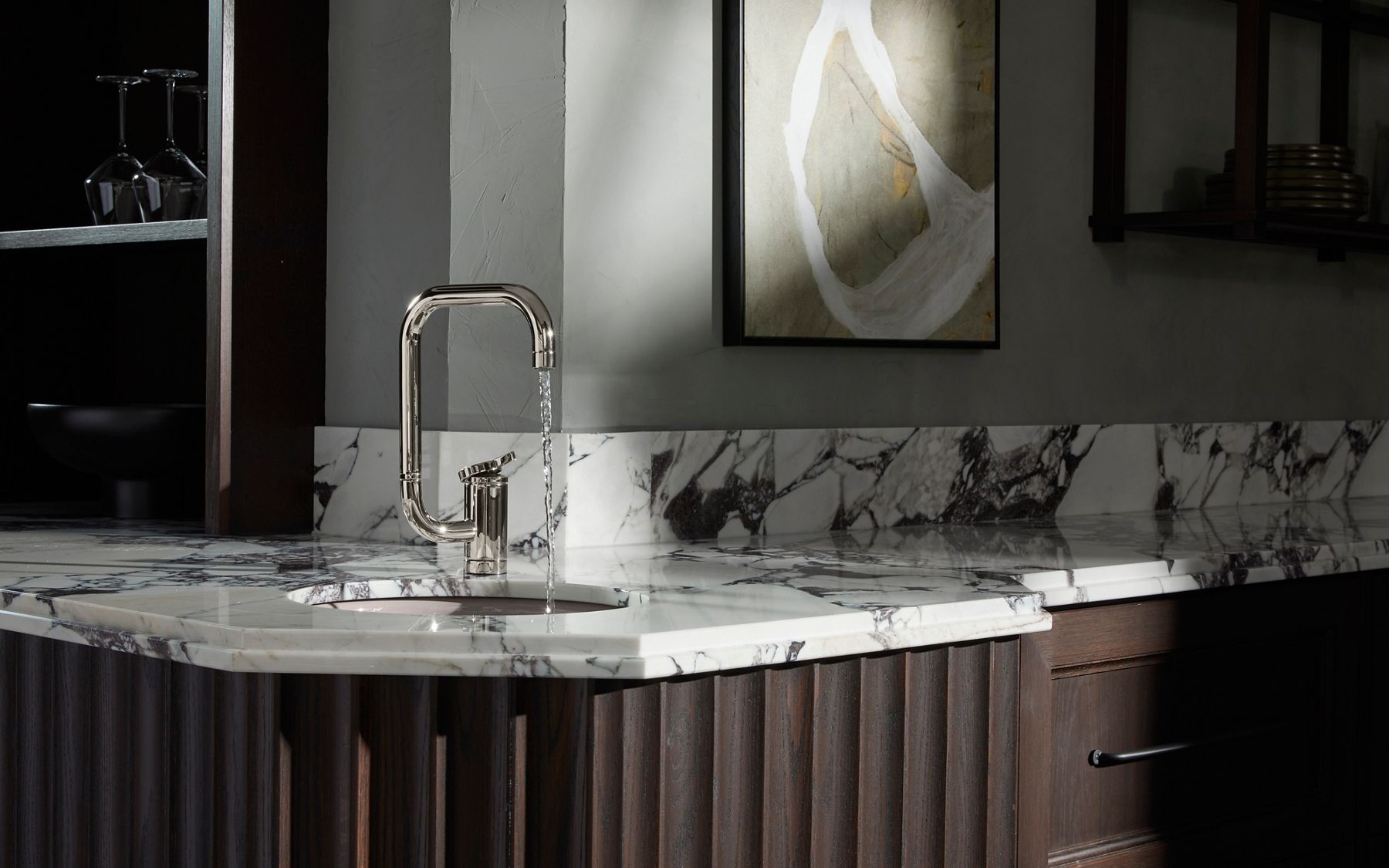 Modern kitchen featuring a unique, rectangular-shaped chrome faucet with water flowing into a sink. The countertop is made of luxurious white marble with dark veining, and the minimalist design highlights the sleek, industrial aesthetic of the space.