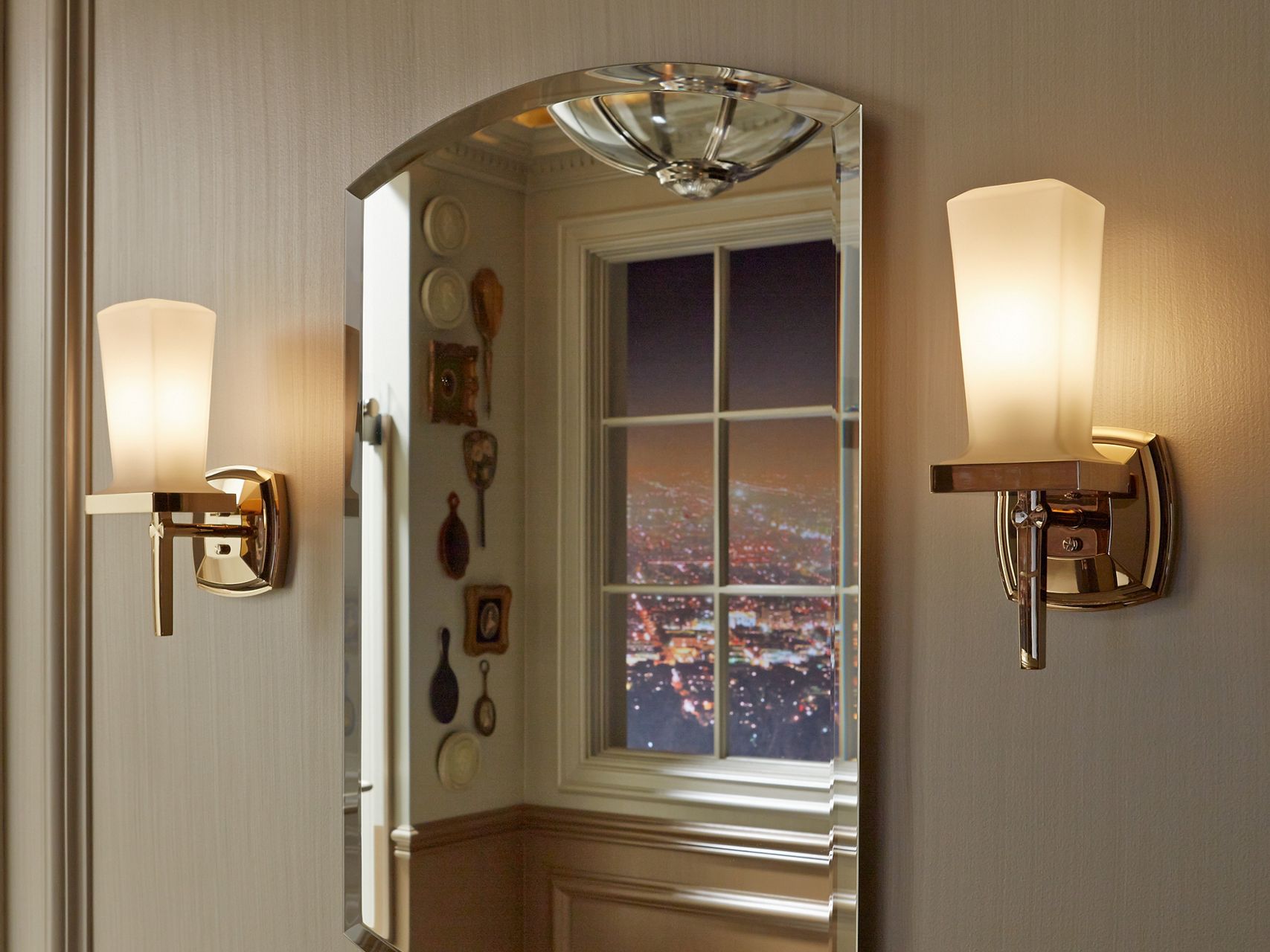 An arched medicine cabinet with a beveled mirror edge hangs in a bathroom between two single-light sconces.