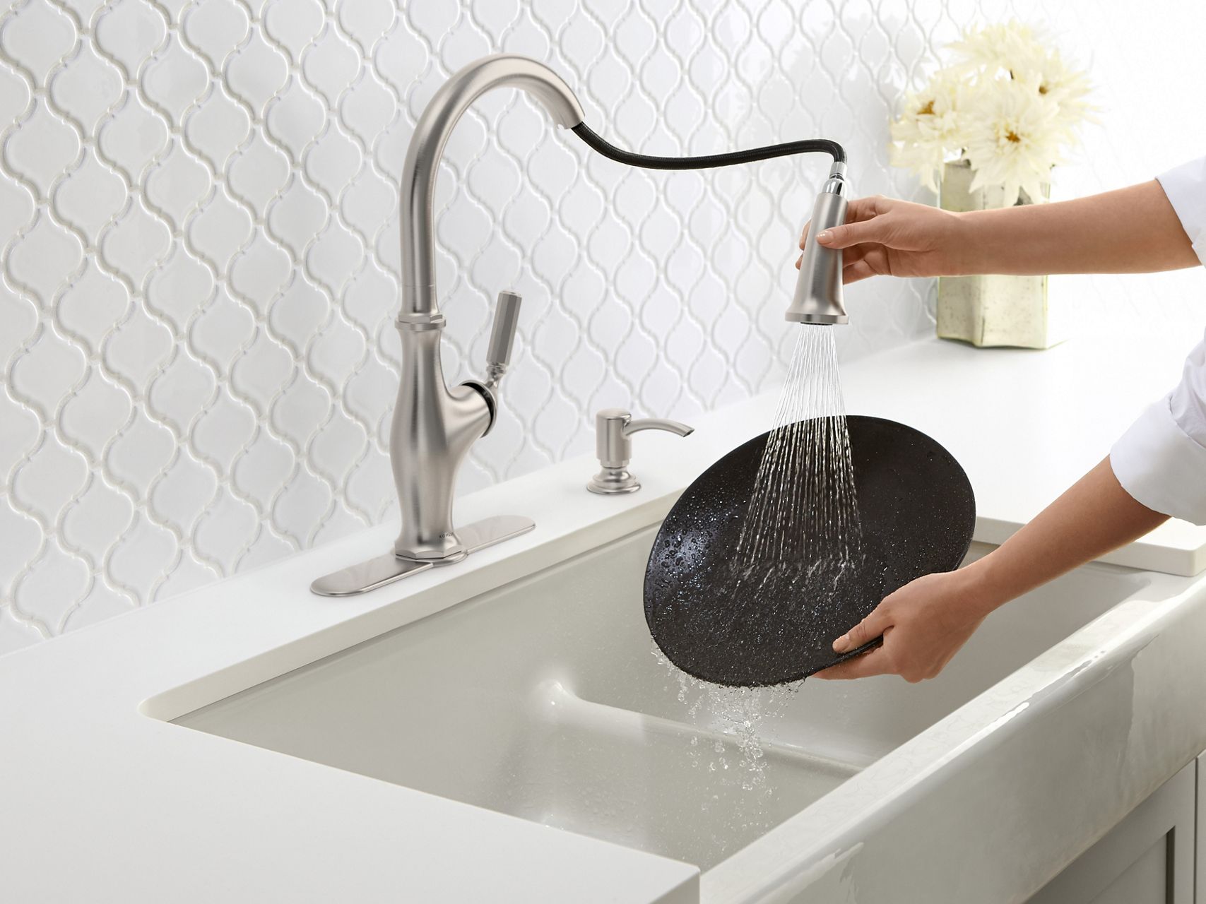 Hands clean a plate with a pull-down kitchen faucet in a Whitehaven Self-Trimming Smart Divide double-bowl kitchen sink with short apron