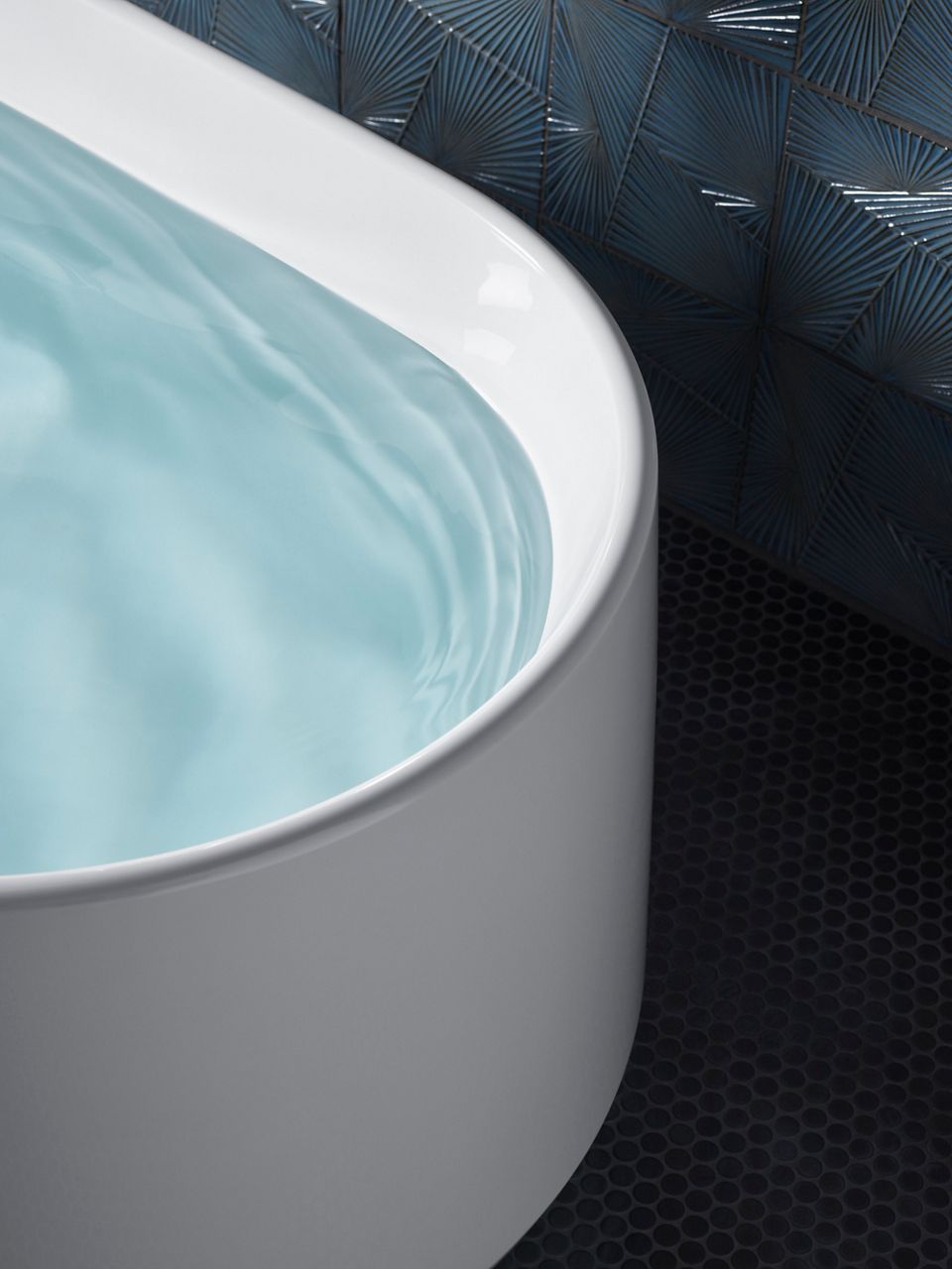 Detail of a freestanding bath filled with water on a dark gray floor.
