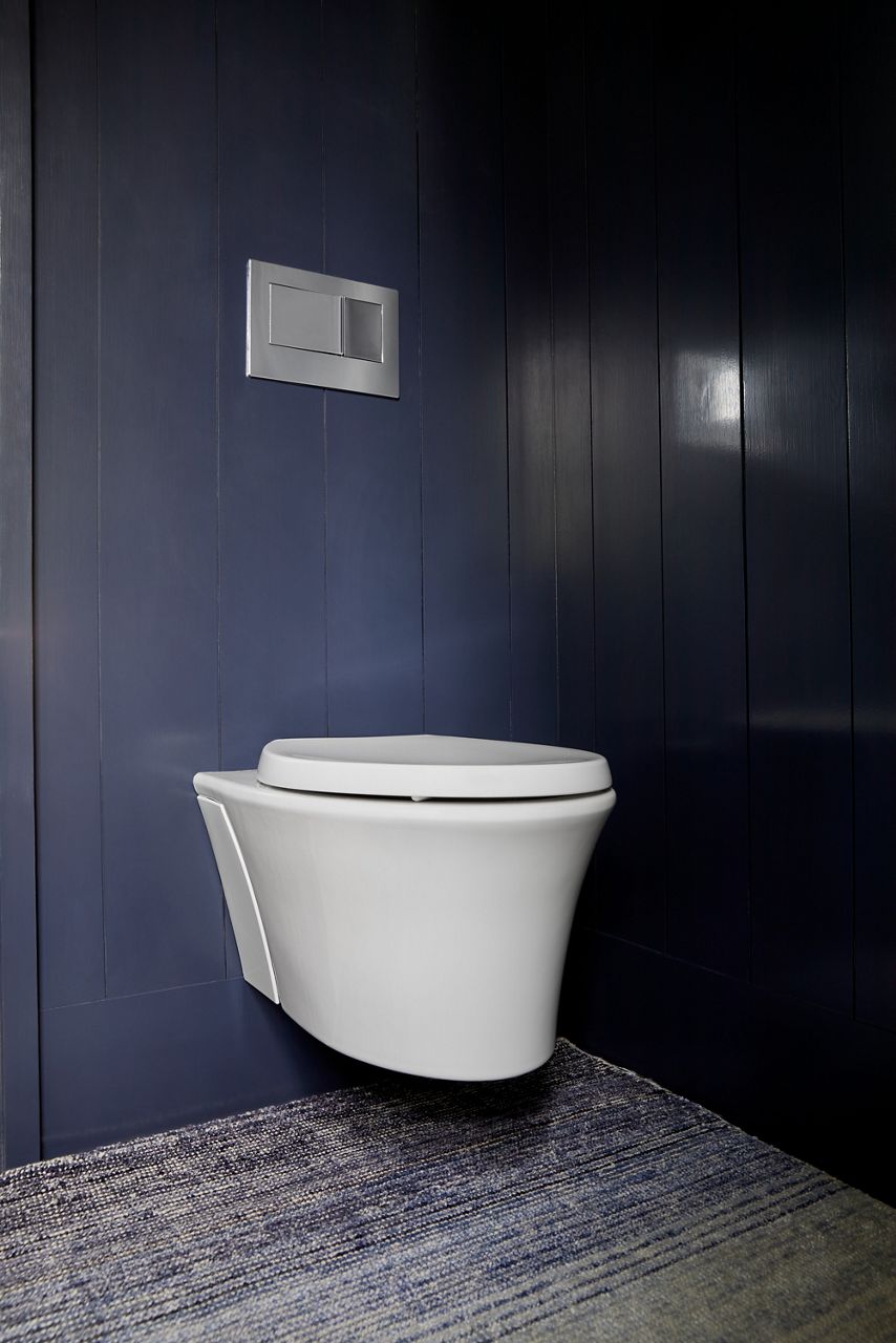 Une salle de bain à installation murale bleu foncé avec toilette murale Veil blanche et tapis neutre à motifs.