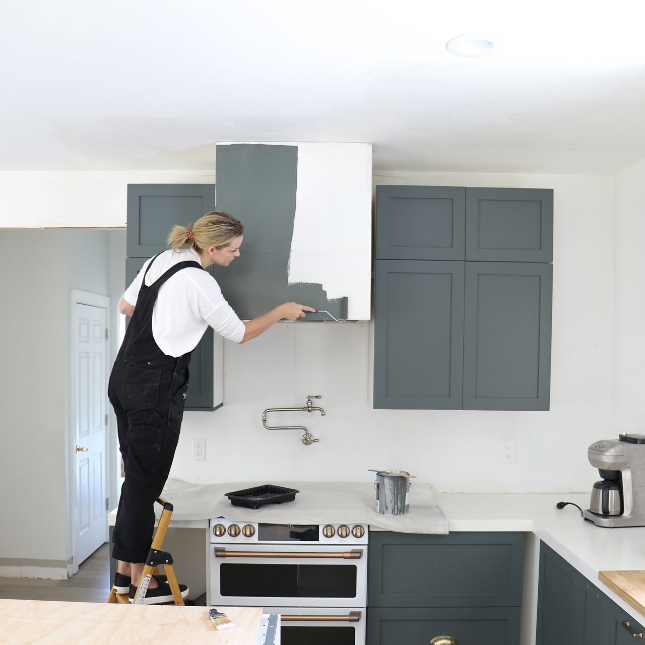 Jennifer Gizzi paints a range hood cover over a stove