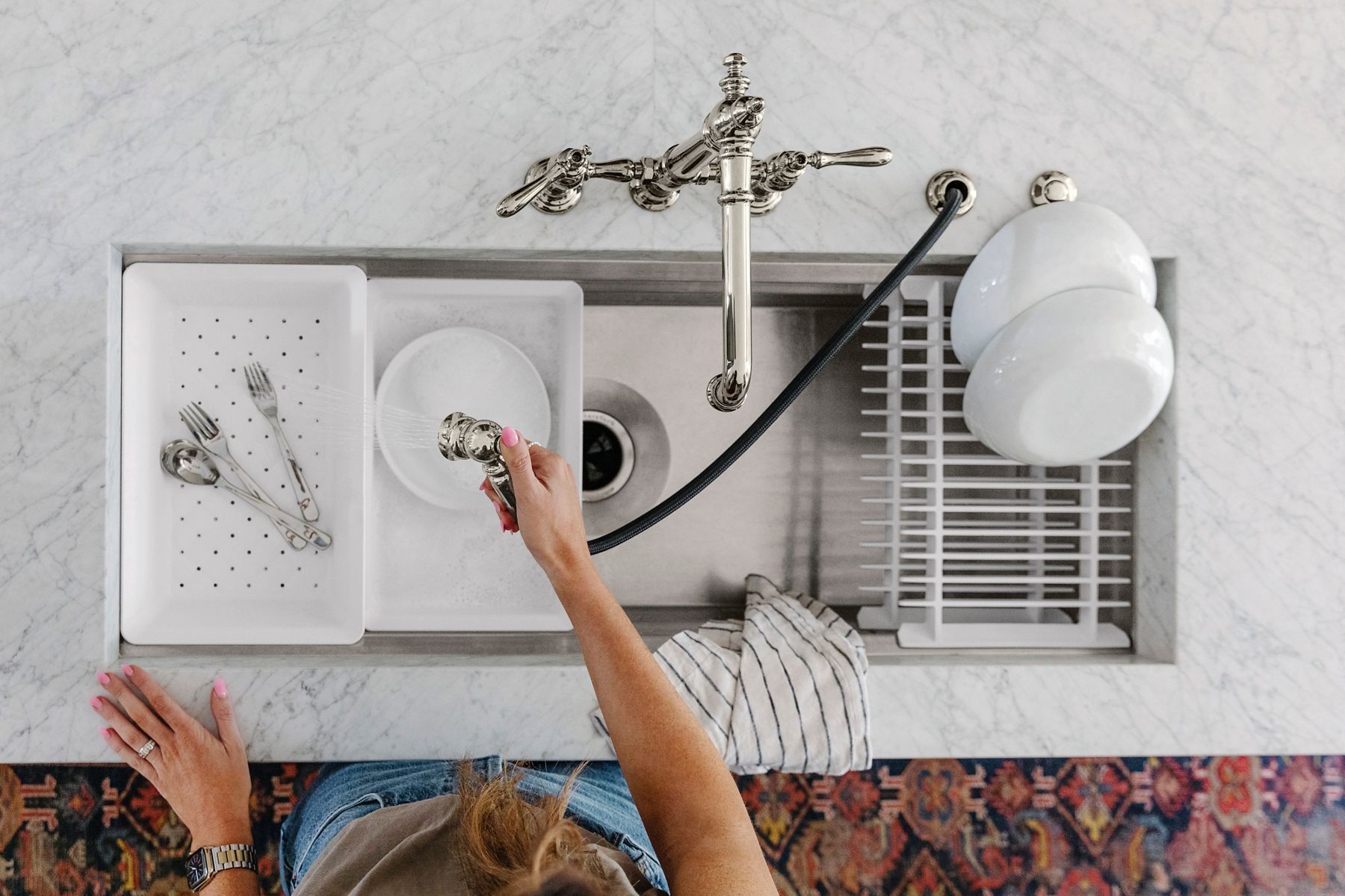 Overhead image of the Kohler Prolific workstation sink installed in the kitchen island, where we see Julia using the hand-spray faucet to wash some dishes in the sink. 