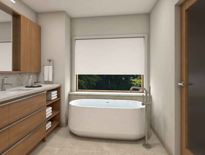 Freestanding bathtub next to vanity with wooden cabinets in a contemporary bathroom with large window and roller shade.