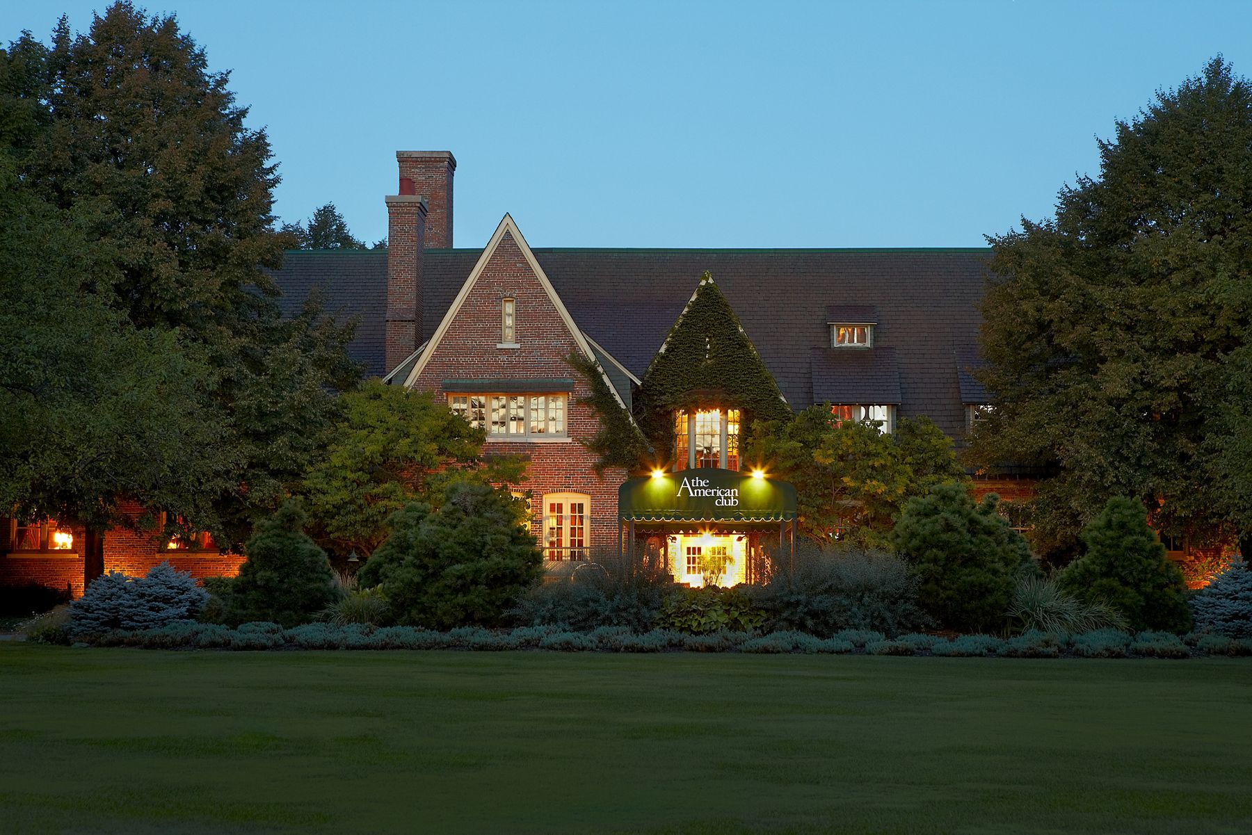 Exterior view of the front entrance of The American Club hotel at dusk with building exerior and interior lights turned on.
