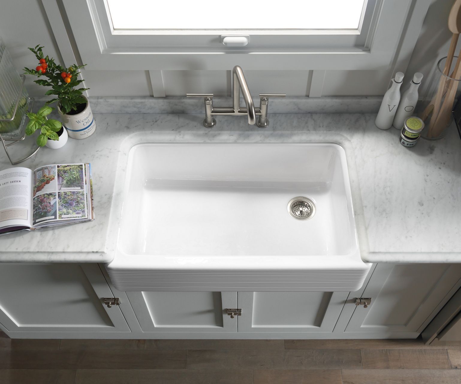 Overhead view of Whitehaven undermount single-bowl kitchen sink with tall apron and Hayridge design set in marble countertops with flowers and a gardening book