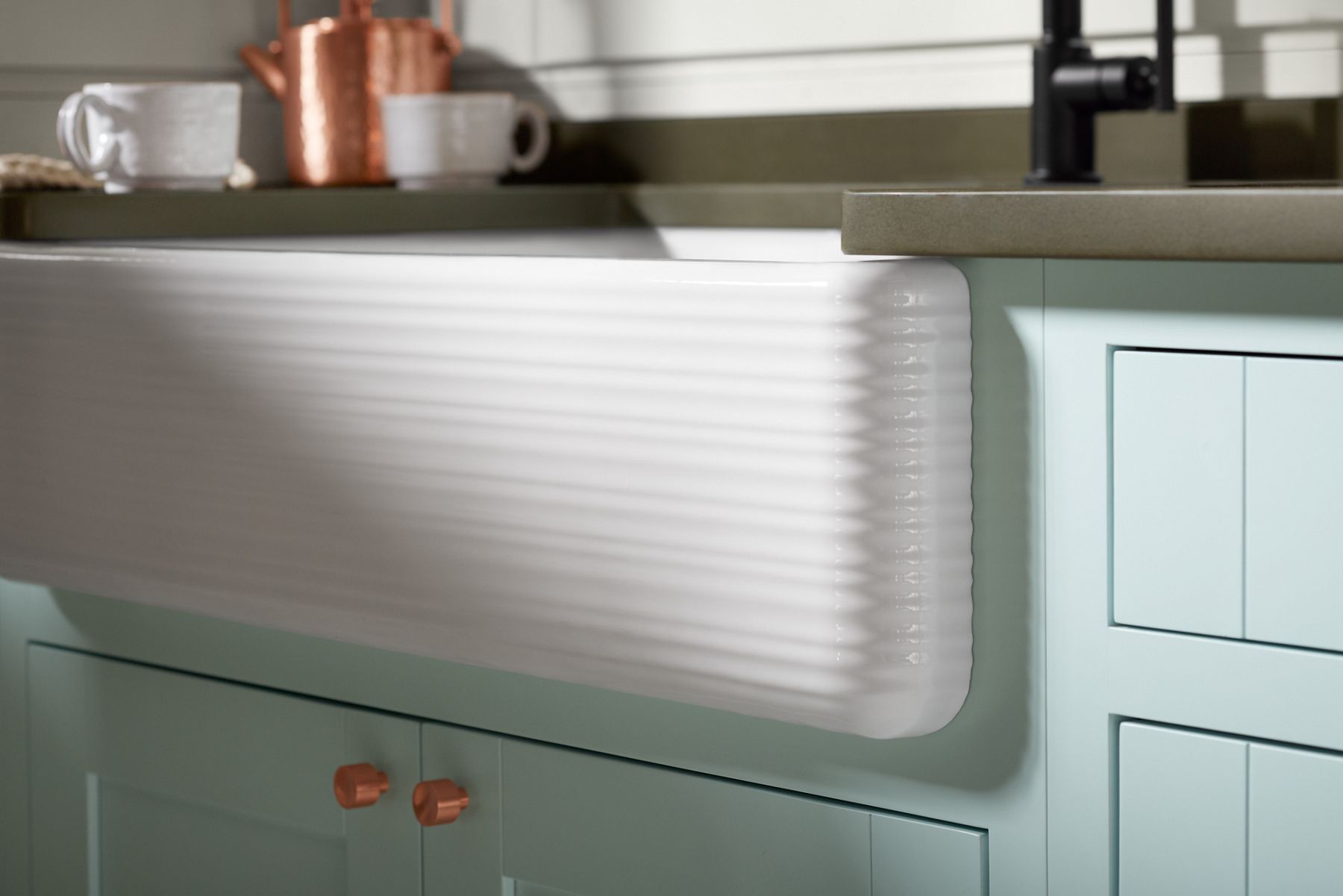 A KOHLER Whitehaven undermount kitchen sink with tall apron and Hayridge design in seafoam green cabinetry and dark countertops