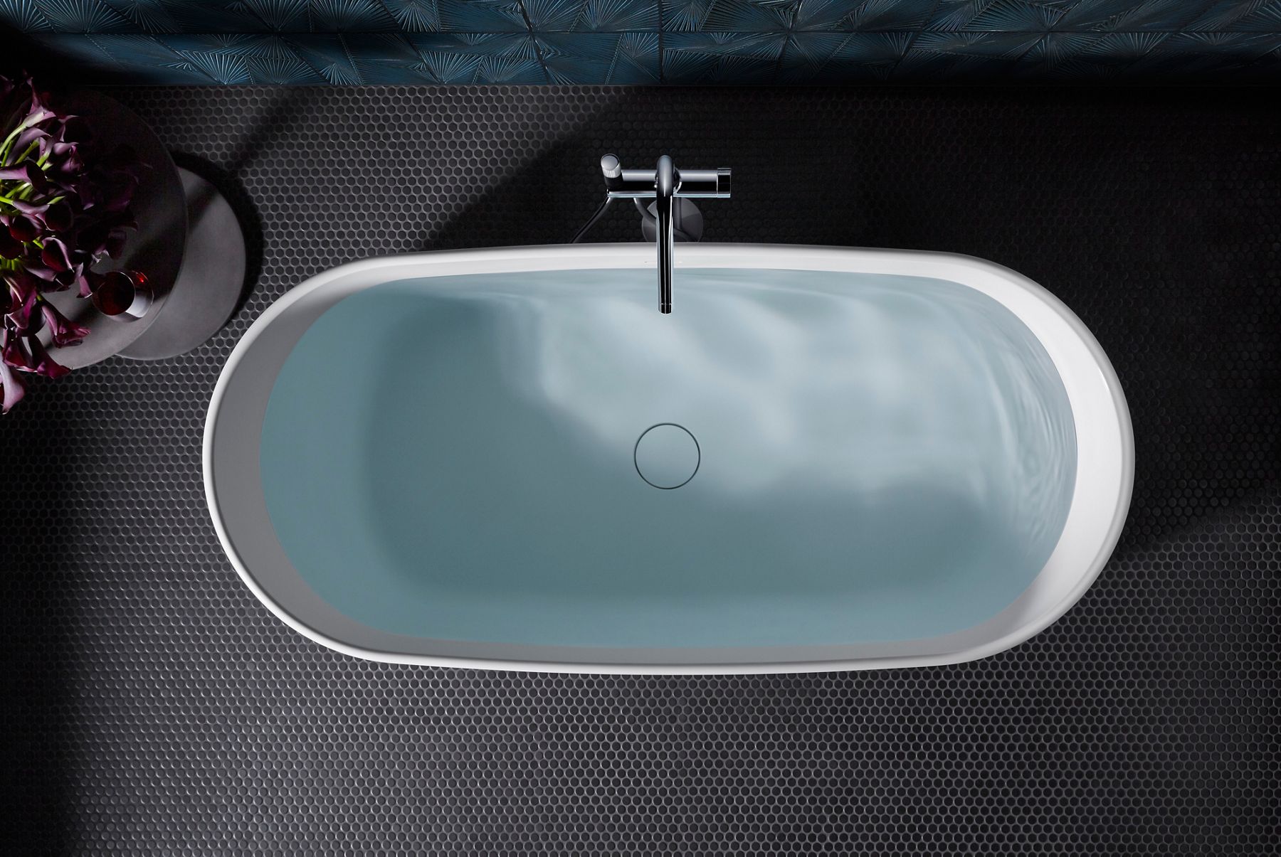 Overhead view of a freestanding bath filled with water on a dark gray floor.