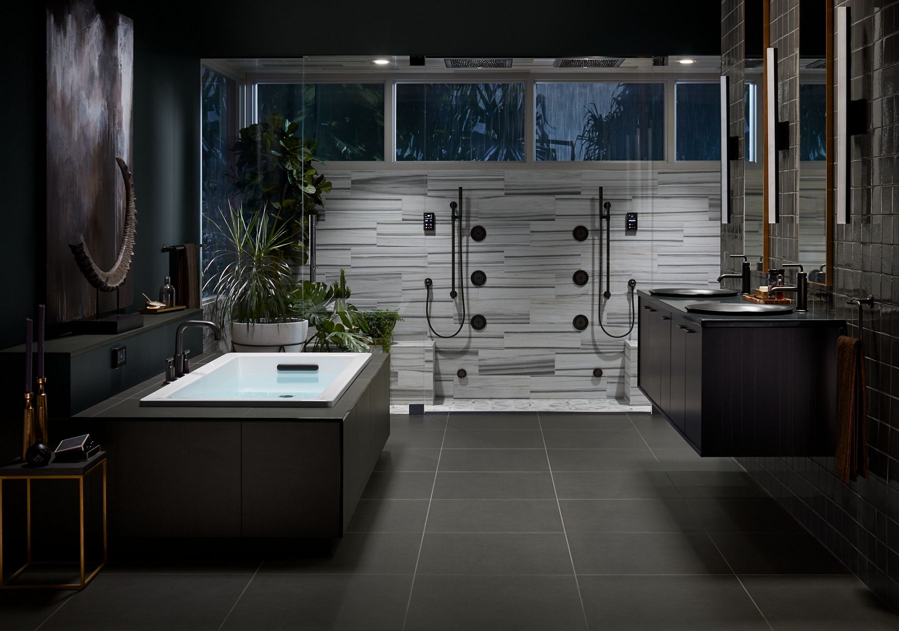 A modern bathroom with a large double shower area in the center background with body sprays and hand showers and striated tile walls in bands of gray, and a floating double vanity on the right.