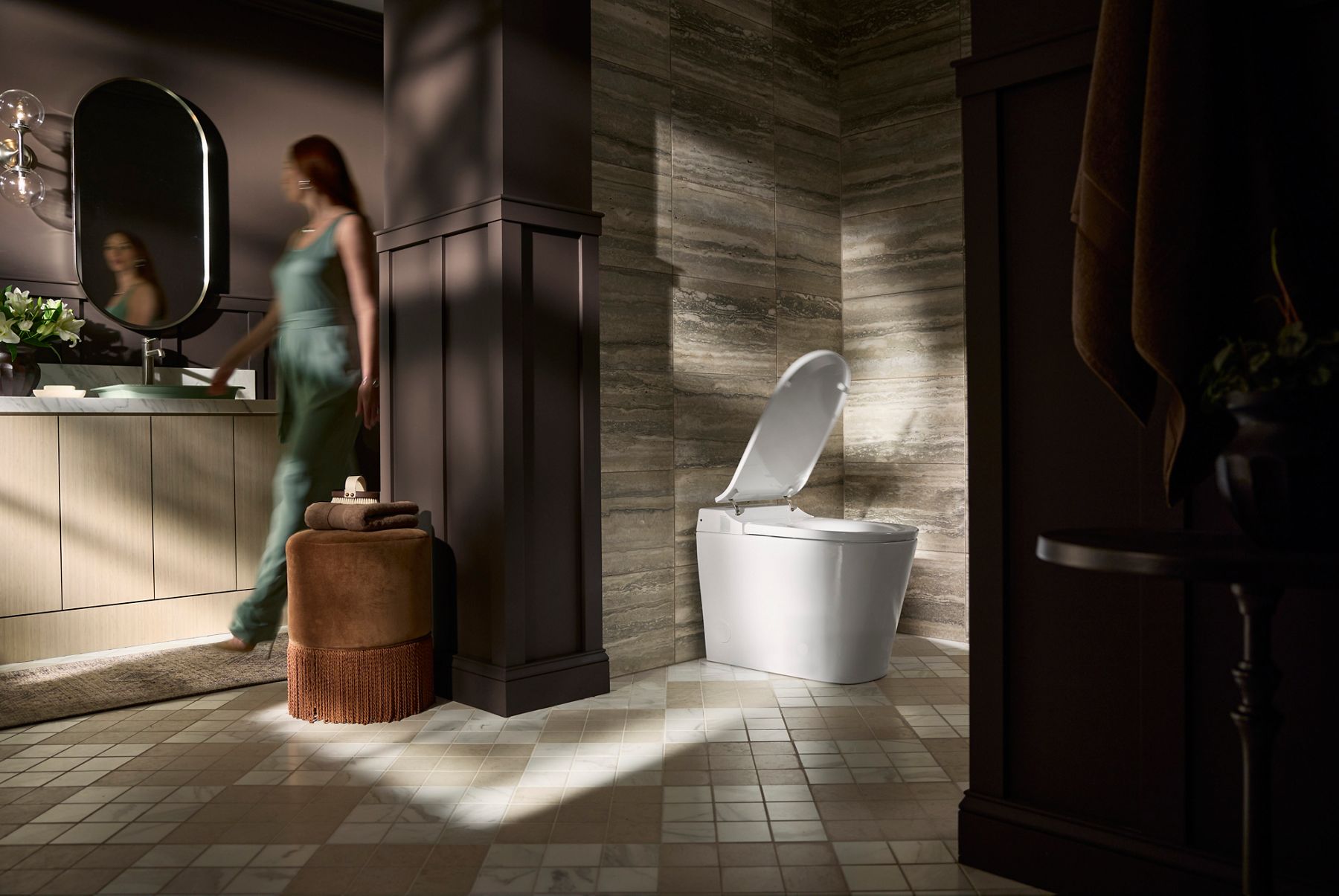 Contemporary bathroom featuring a smart toilet with open lid, stone wall panels, vanity area, and cushioned stool with towels.