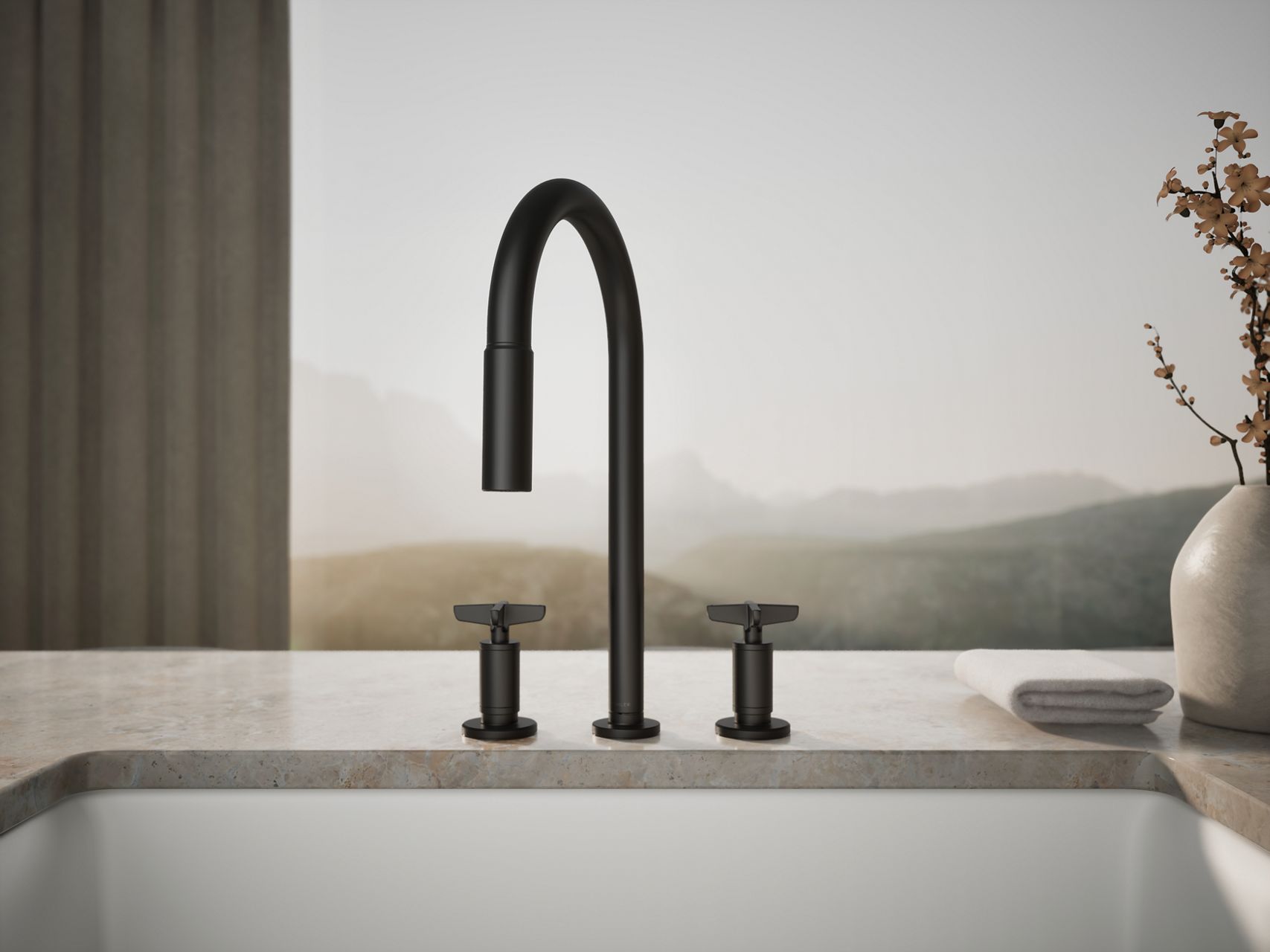 Matte black bridge kitchen faucet with curved spout mounted on a light stone countertop beside a white sink, with a soft landscape backdrop and ceramic vase styling.
