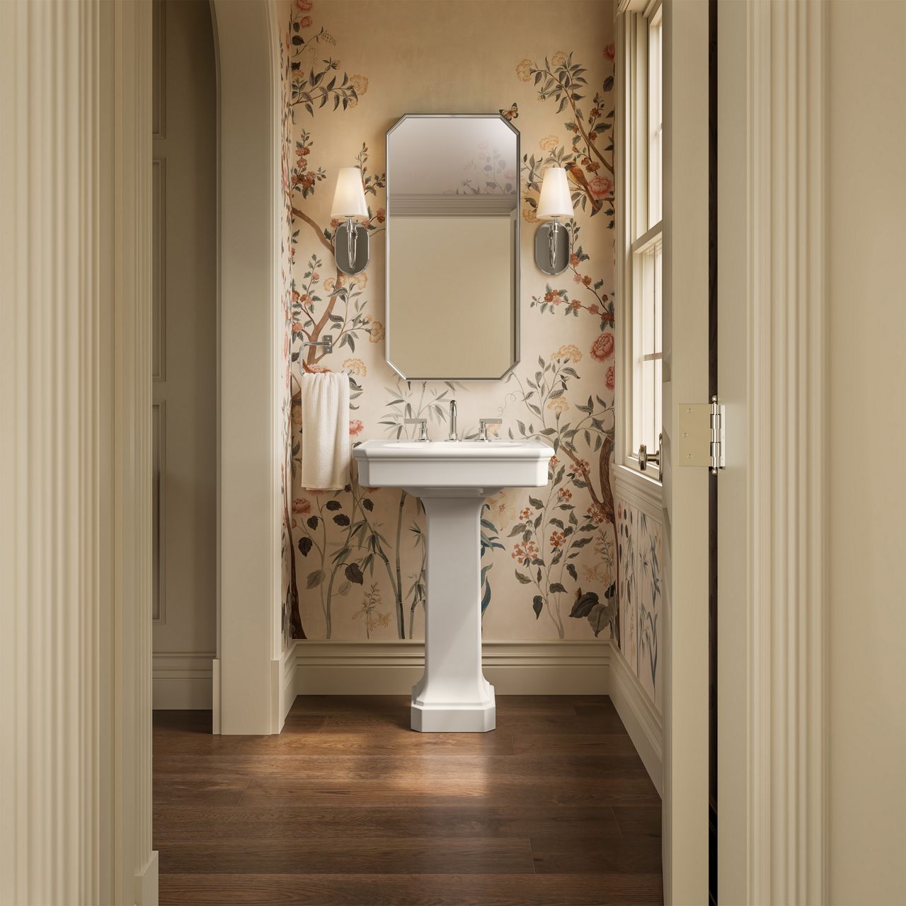 Pedestal sink and decorative mirror with wall sconces set against floral wallpaper in a classic powder room.