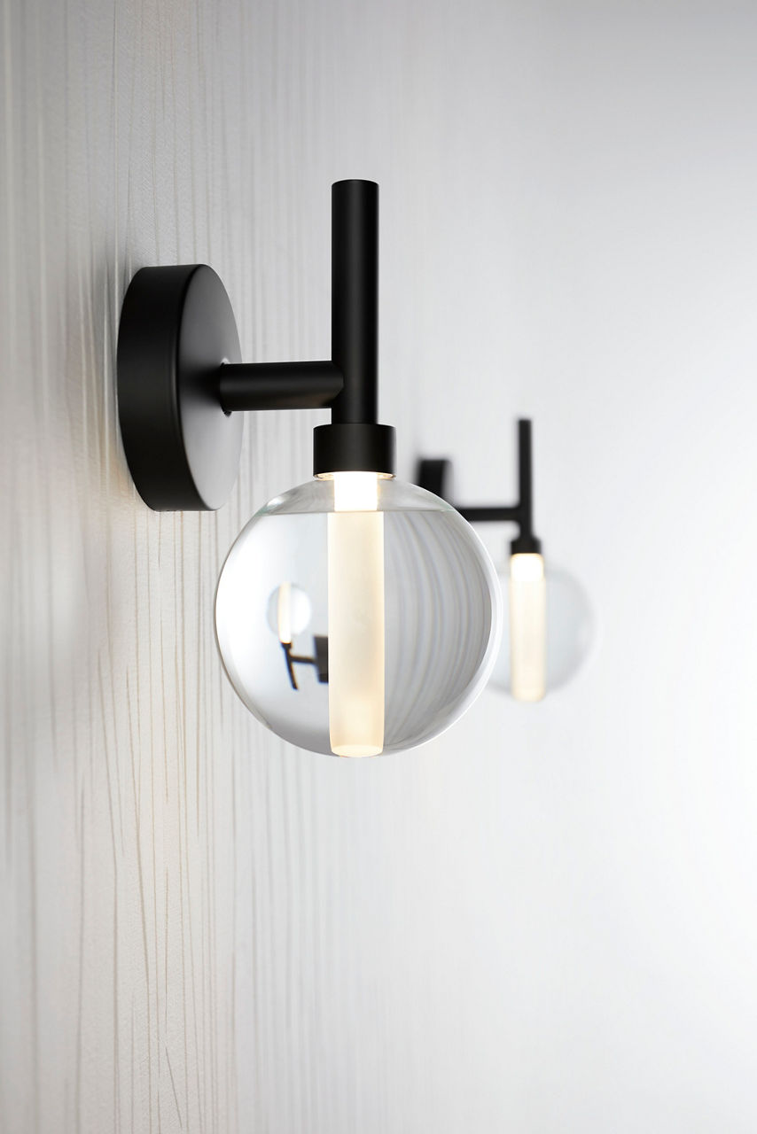 Modern matte black wall sconce with clear globe glass shade and exposed bulb against a white wall.
