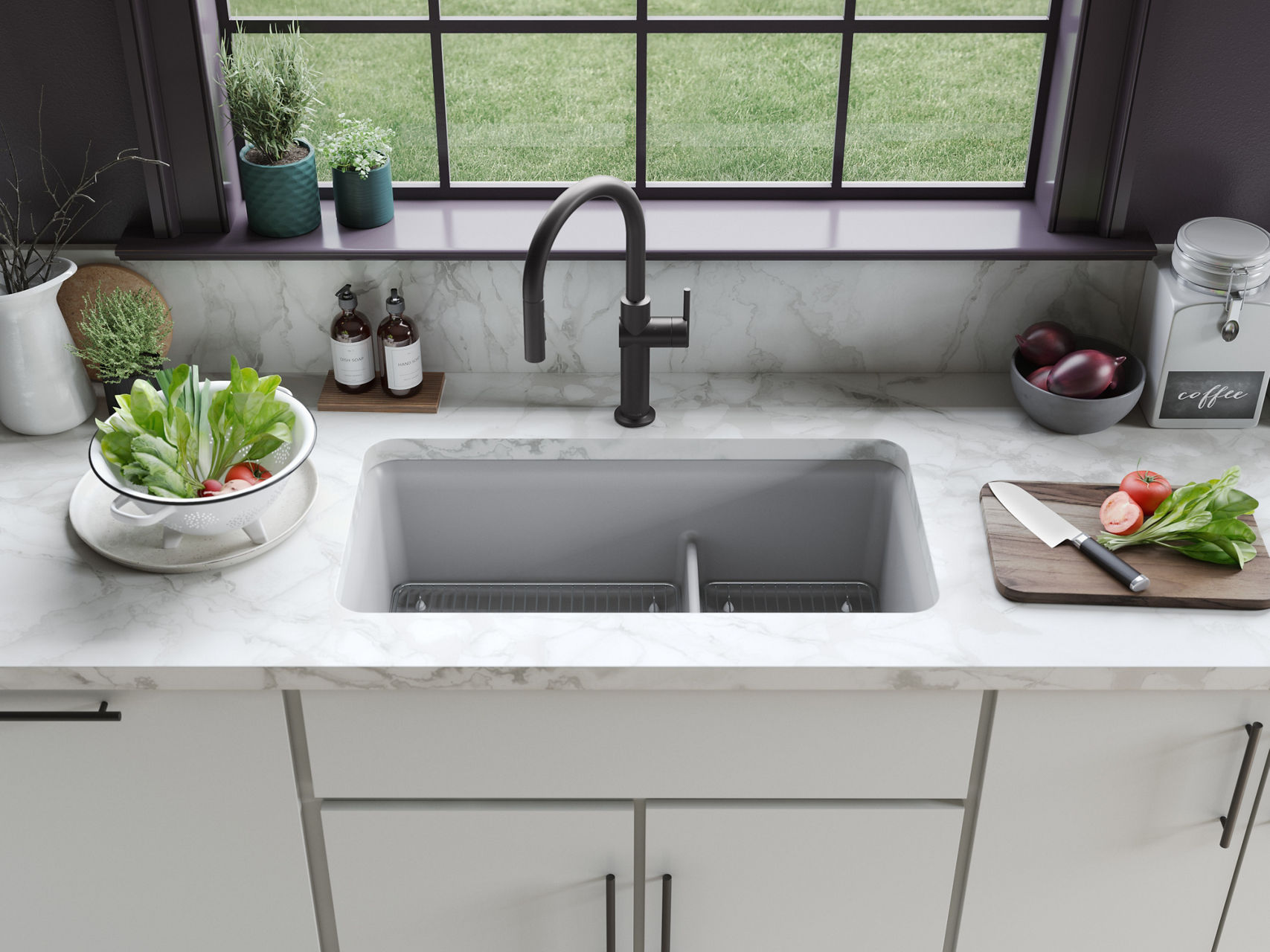 Double-basin concrete=look sink with matte black faucet, placed beneath a window and surrounded by fresh produce.