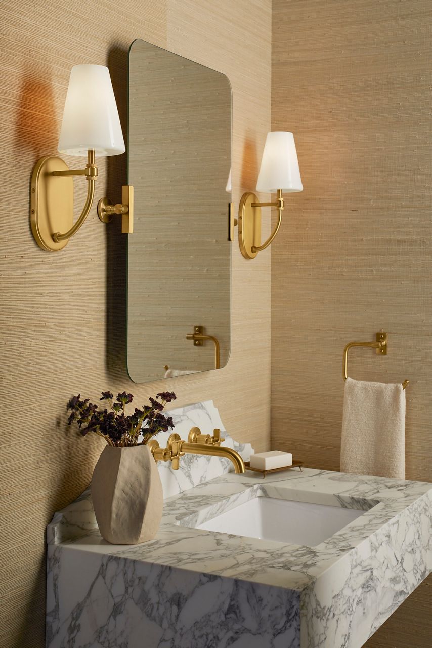 Castia collection bathroom vanity featuring a marble countertop, undermount sink, brushed gold faucet, and matching wall sconces flanking a rounded rectangular mirror.