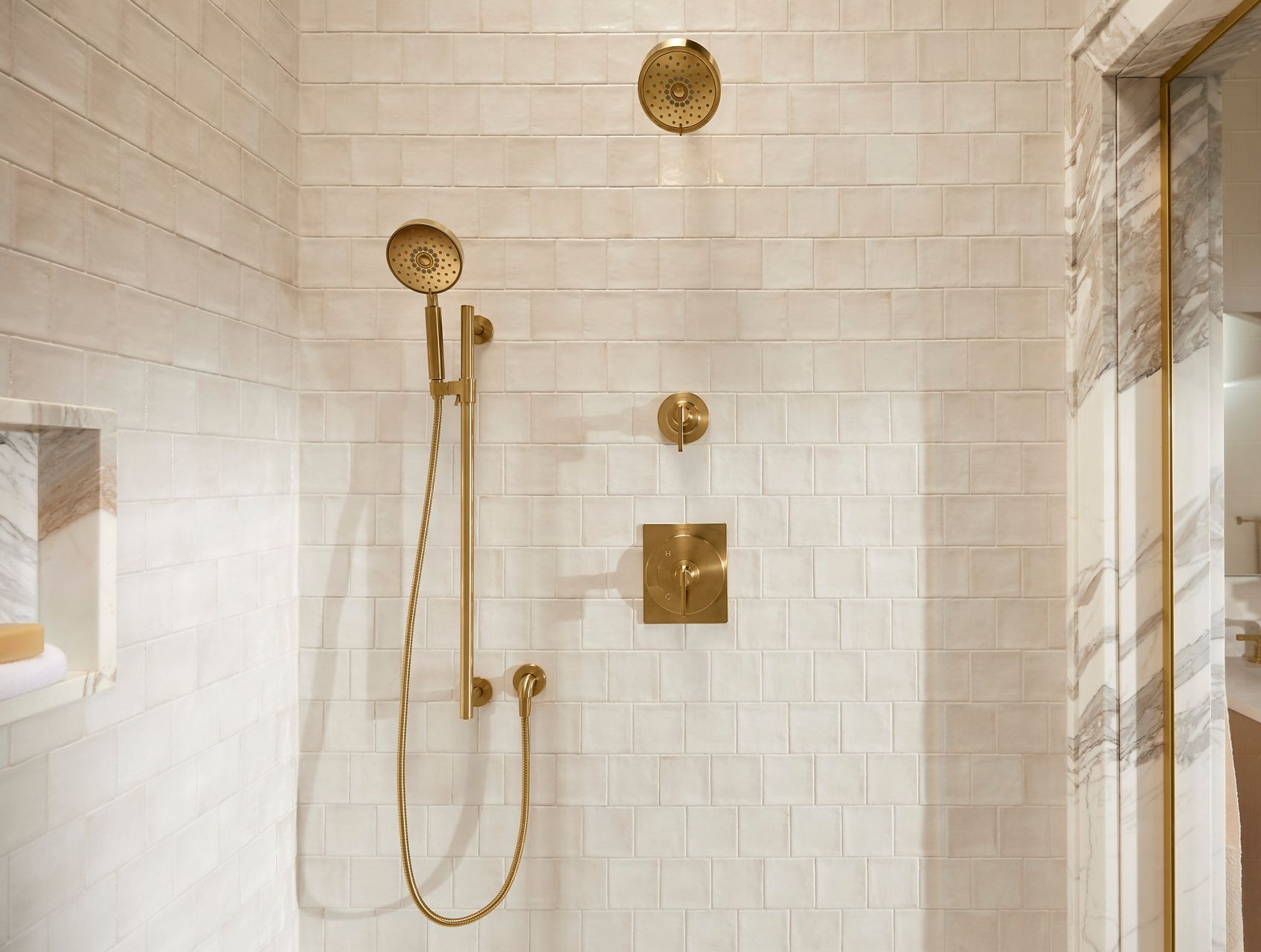 Castia collection walk-in shower featuring brushed gold shower fixtures, including a rainhead and handshower, set against light textured tile walls.