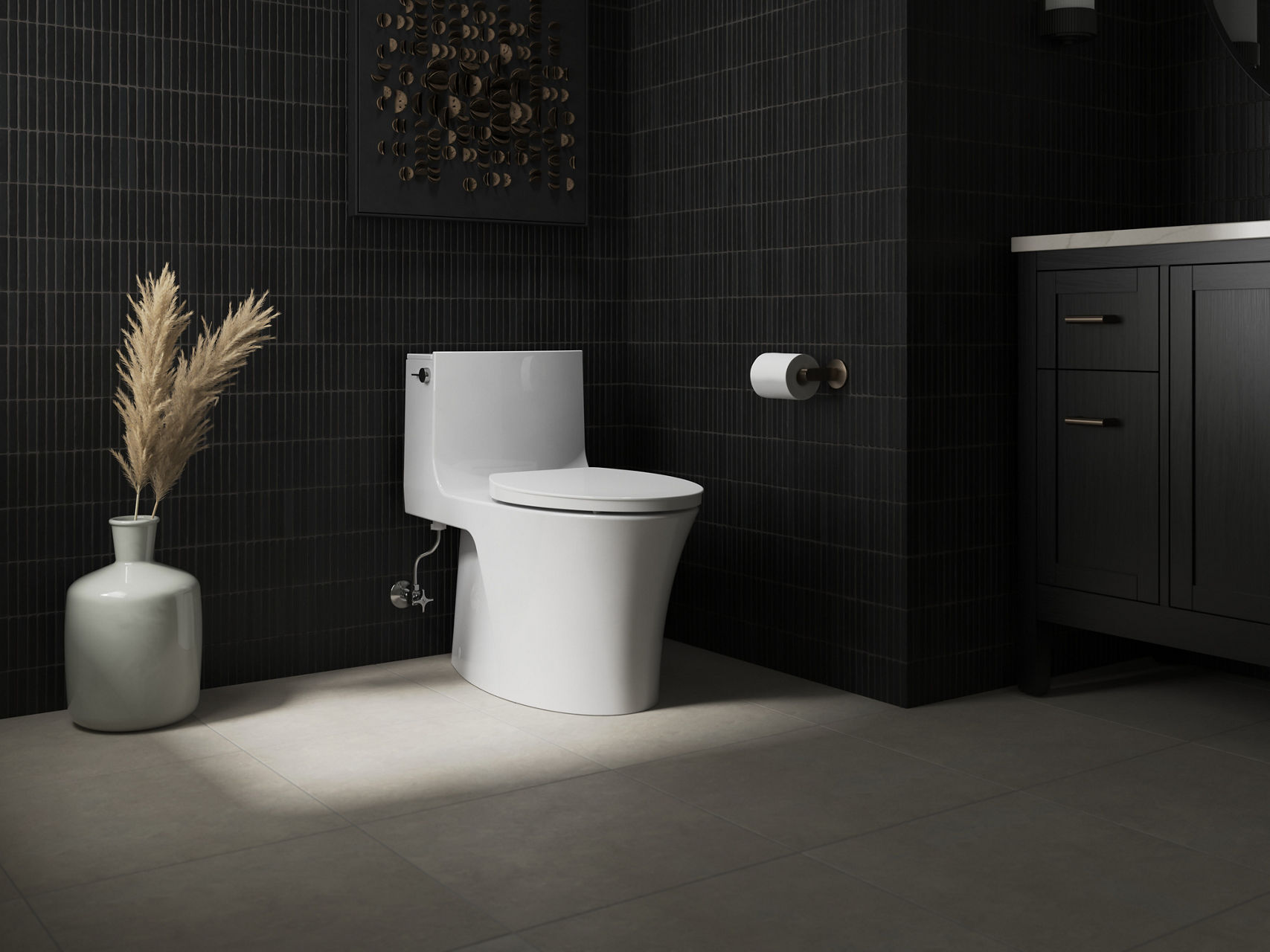 Sleek white toilet in a dark minimalist bathroom with black tile walls and decorative pampas grass.