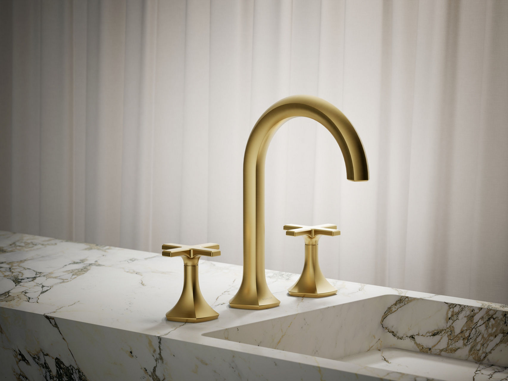 Brushed gold faucet with tall curved gooseneck spout and tapered dual handles on stone countertop.