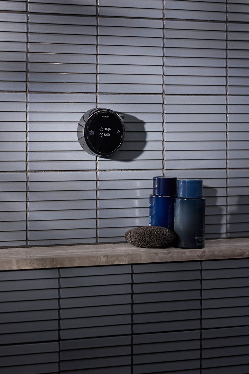 Decorative bathroom vignette featuring textured gray wall tile, a floating stone shelf, dark blue glass vessels, and a round black wall accent.