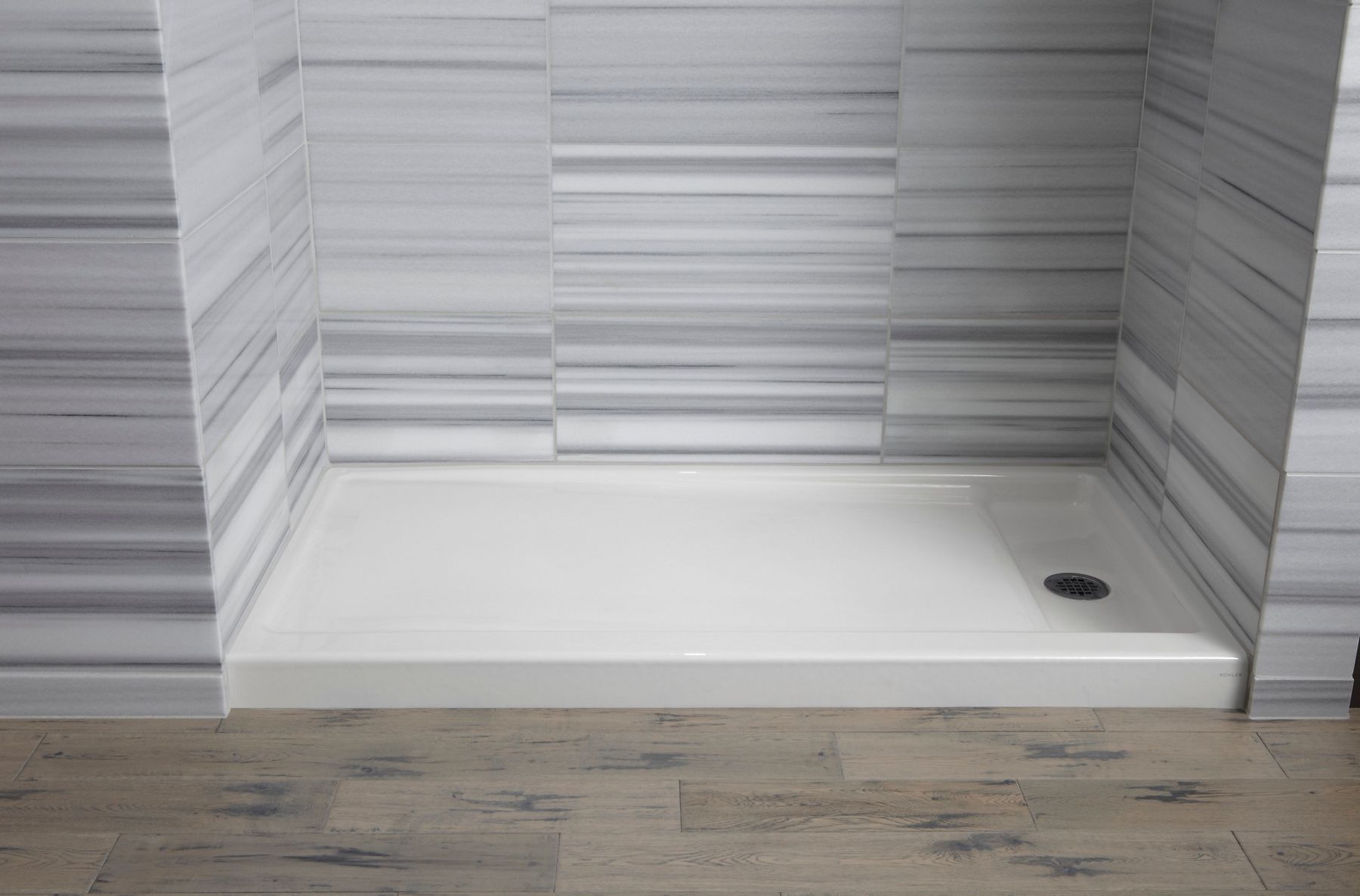  White rectangular shower base installed with gray linear wall tile and wood-look flooring in a modern shower space.