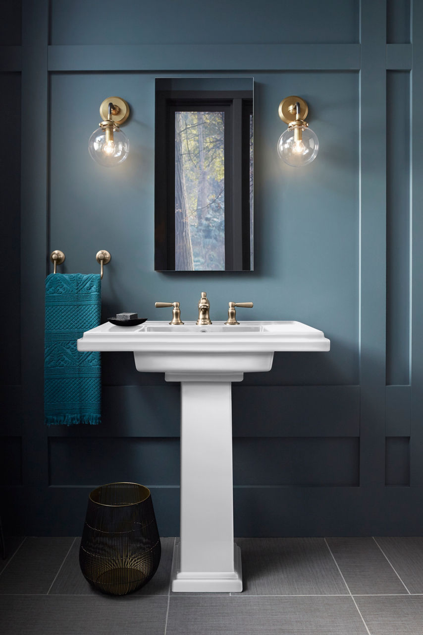 Classic pedestal sink with dual-handle faucet in a white finish, placed against a blue wall with a mirror above