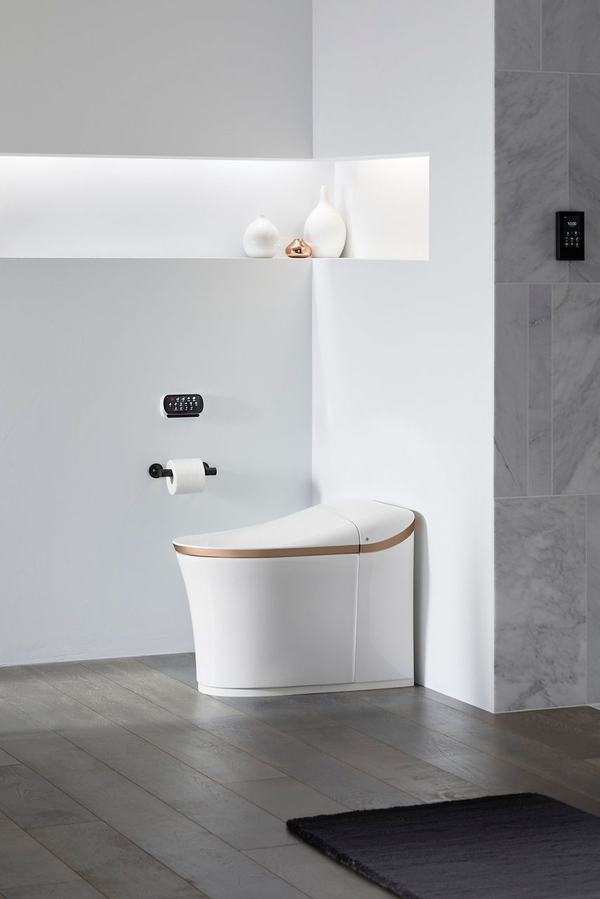 Modern white smart toilet with integrated bidet features in a minimalist bathroom with recessed shelving and dark wood flooring.
