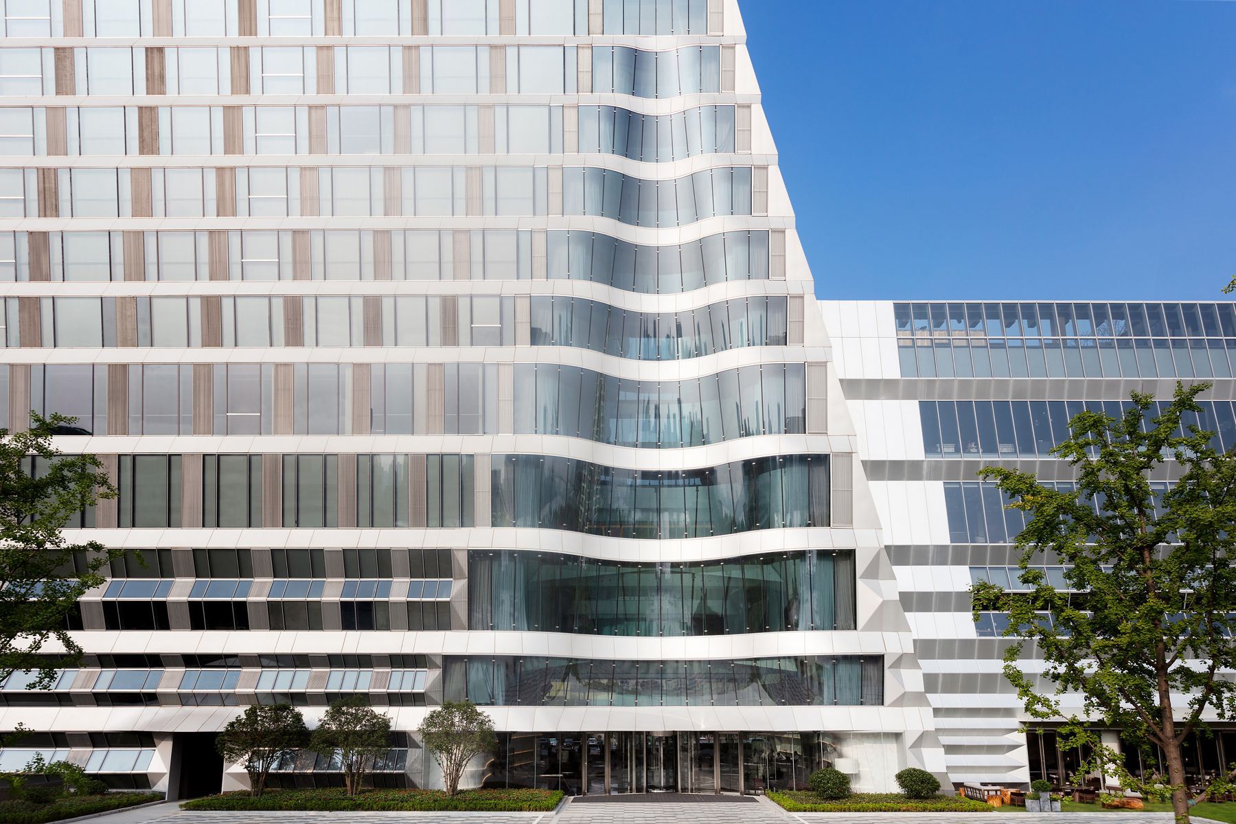 The exterior of a hotel with a rippling glass structure at the center.